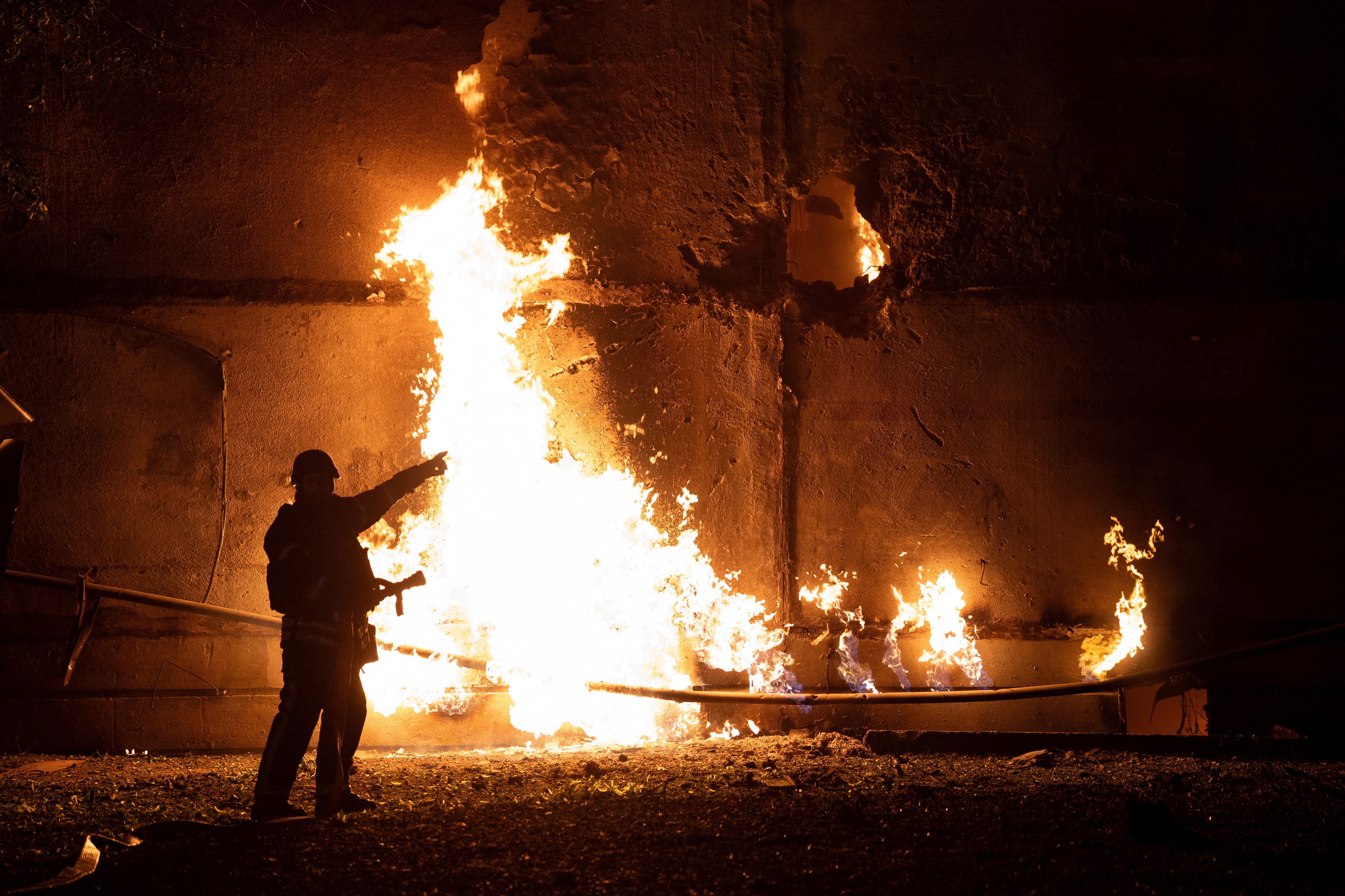 A firefighter stands by a fire and points to a hole following a drone strike in Kharkiv