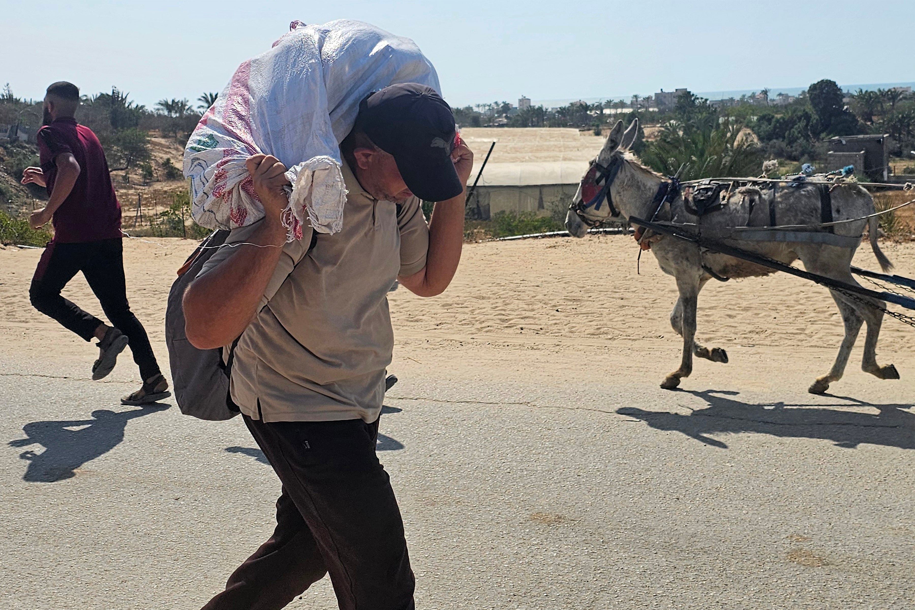 A man walks with a sack on the back of his neck as displaced Palestinians receive humanitarian aid in Rafah