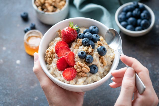 <p>Oatmeal porridge bowl with berry fruits in female hands, closeup view. Healthy vegetarian breakfast food</p>