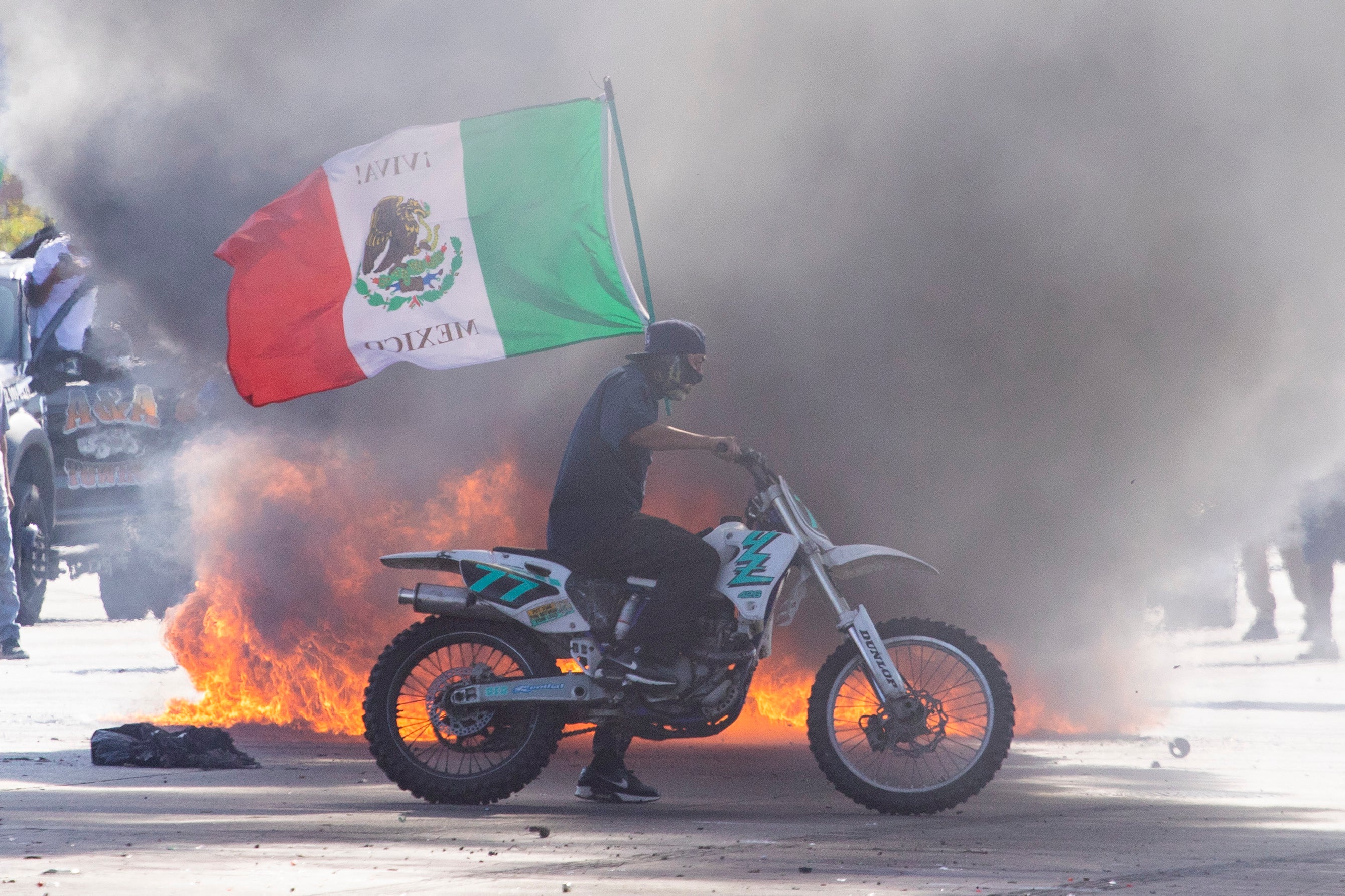 A demonstrator waves a Mexican national flag next to a car on fire during a protest following federal immigration operations, in the Compton neighborhood of Los Angeles, California on June 7, 2025