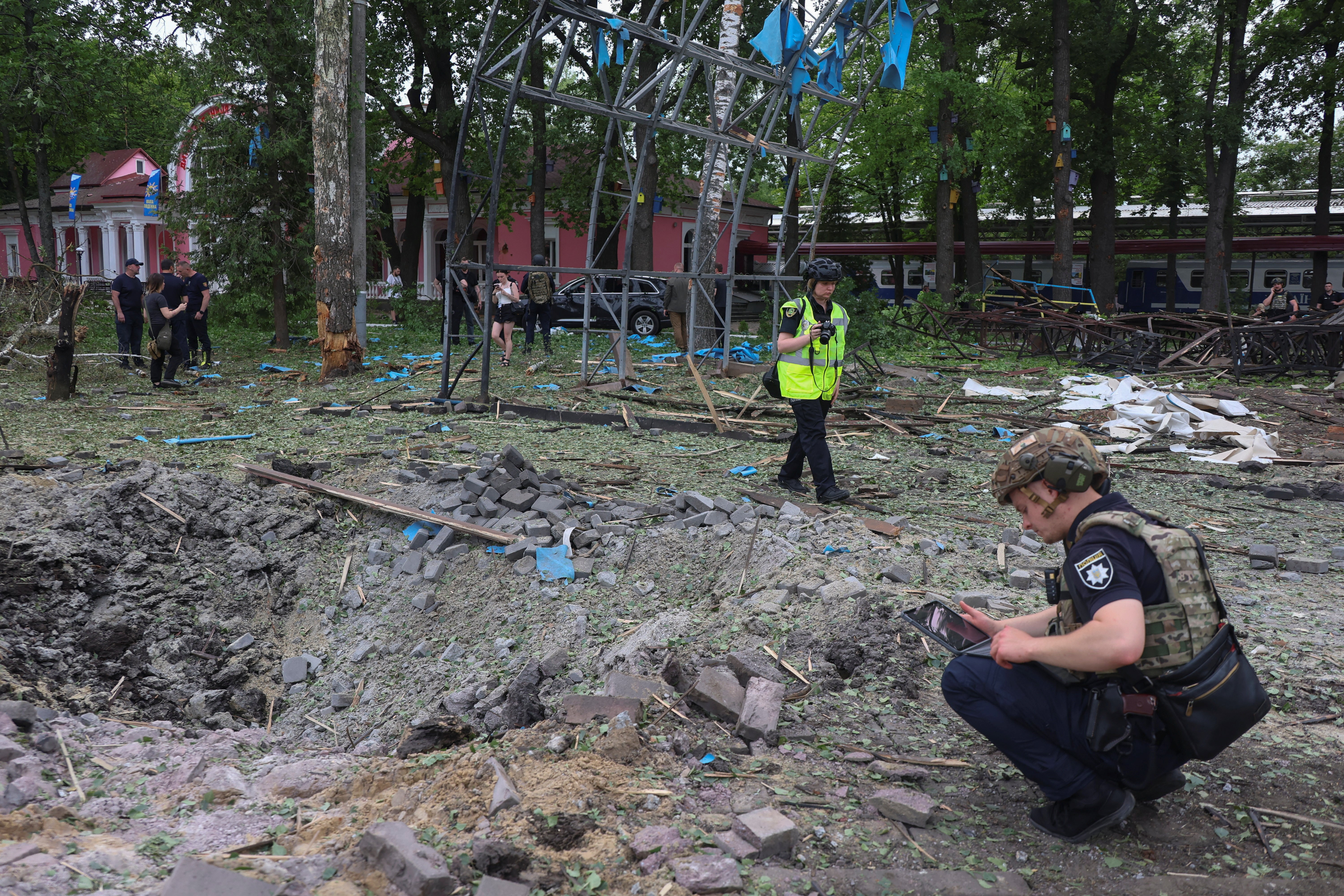 Police officers inspect a crater that appeared after a Russian air strike at a compound in Children's Railway in a park