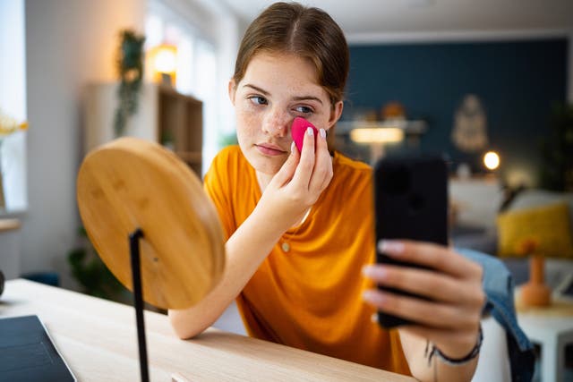 <p>Teenage girl texting messages on her phone while doing make-up.</p>
