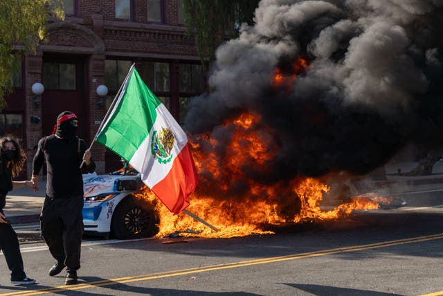 <p>Un manifestante ondea una bandera mexicana frente a un vehículo en llamas durante una protesta en Los Ángeles</p>