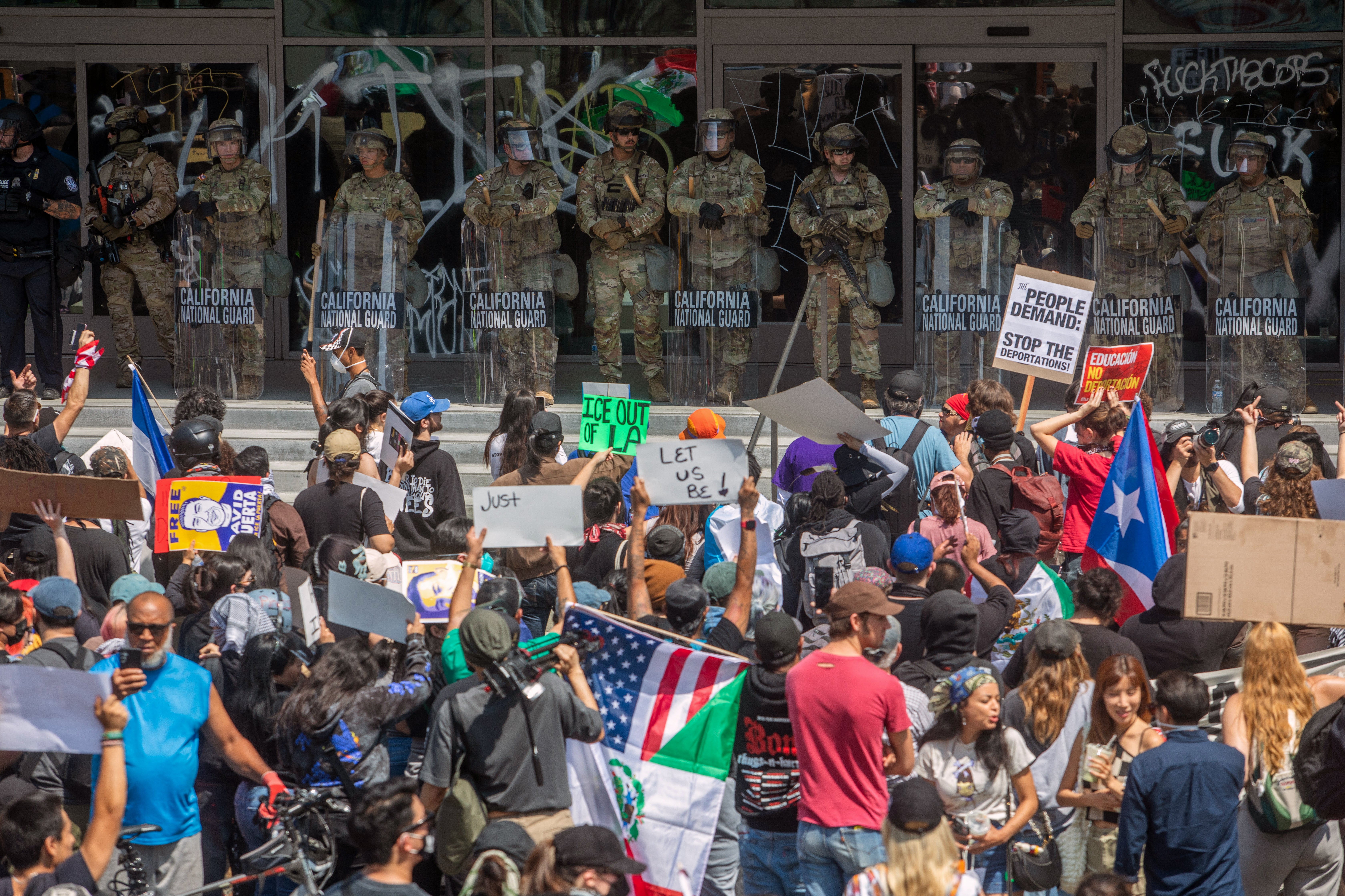 Demonstrators hold signs and flags face California National Guard members standing guard outside the Federal Building as they protest in response to federal immigration operations in Los Angeles, on June 9, 2025.