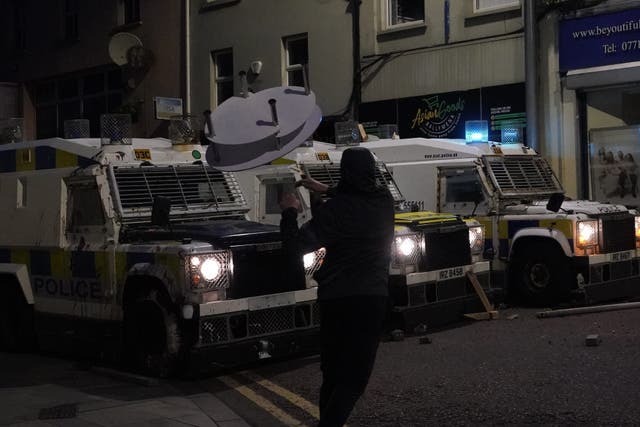 A demonstrator throws a glass table at PSNI vehicles during violence in Ballymena on Tuesday (Niall Carson/PA)