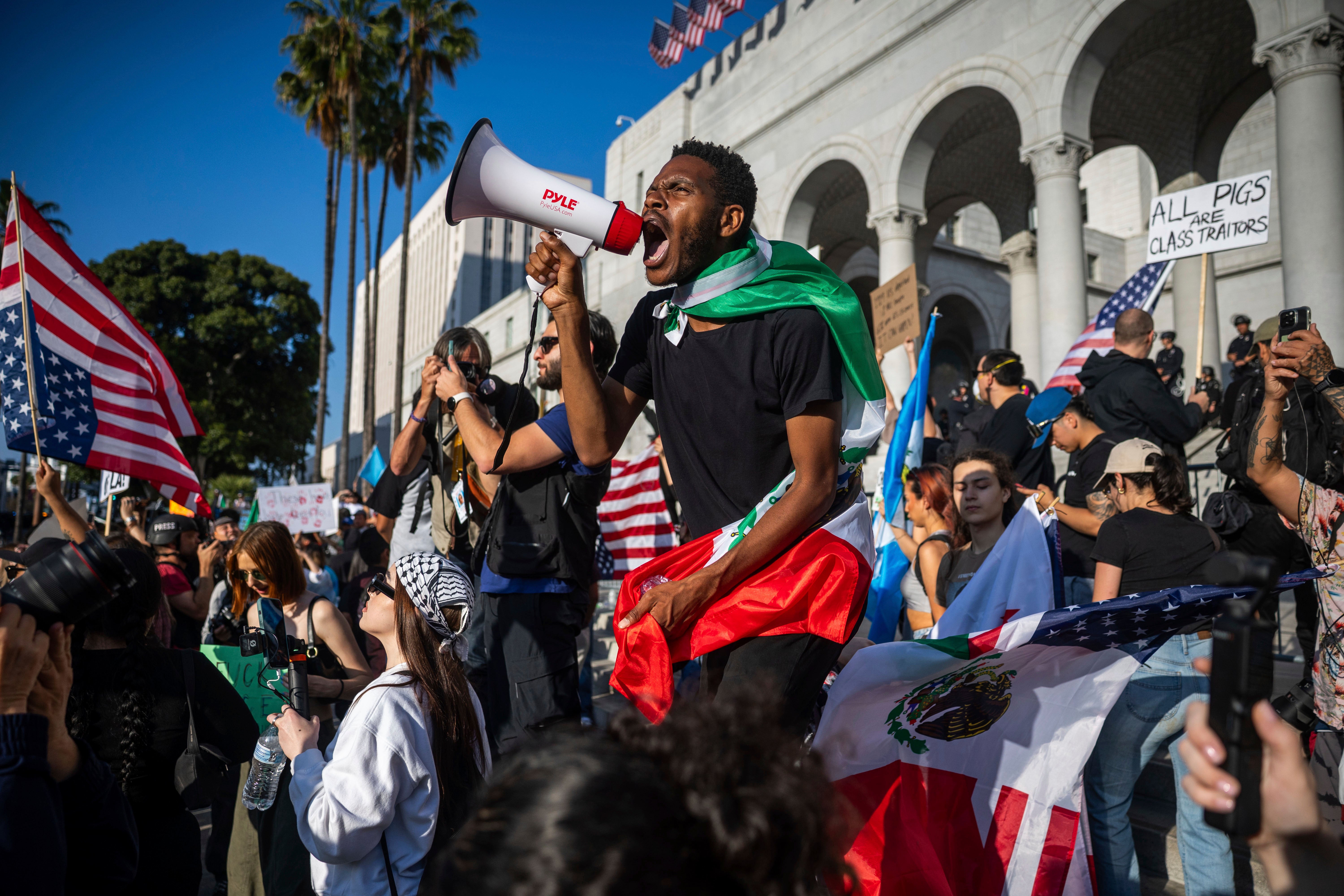 <p>A man shouts into a megaphone outside City Hall during protests over federal immigration enforcement raids on Wednesday in LA</p>