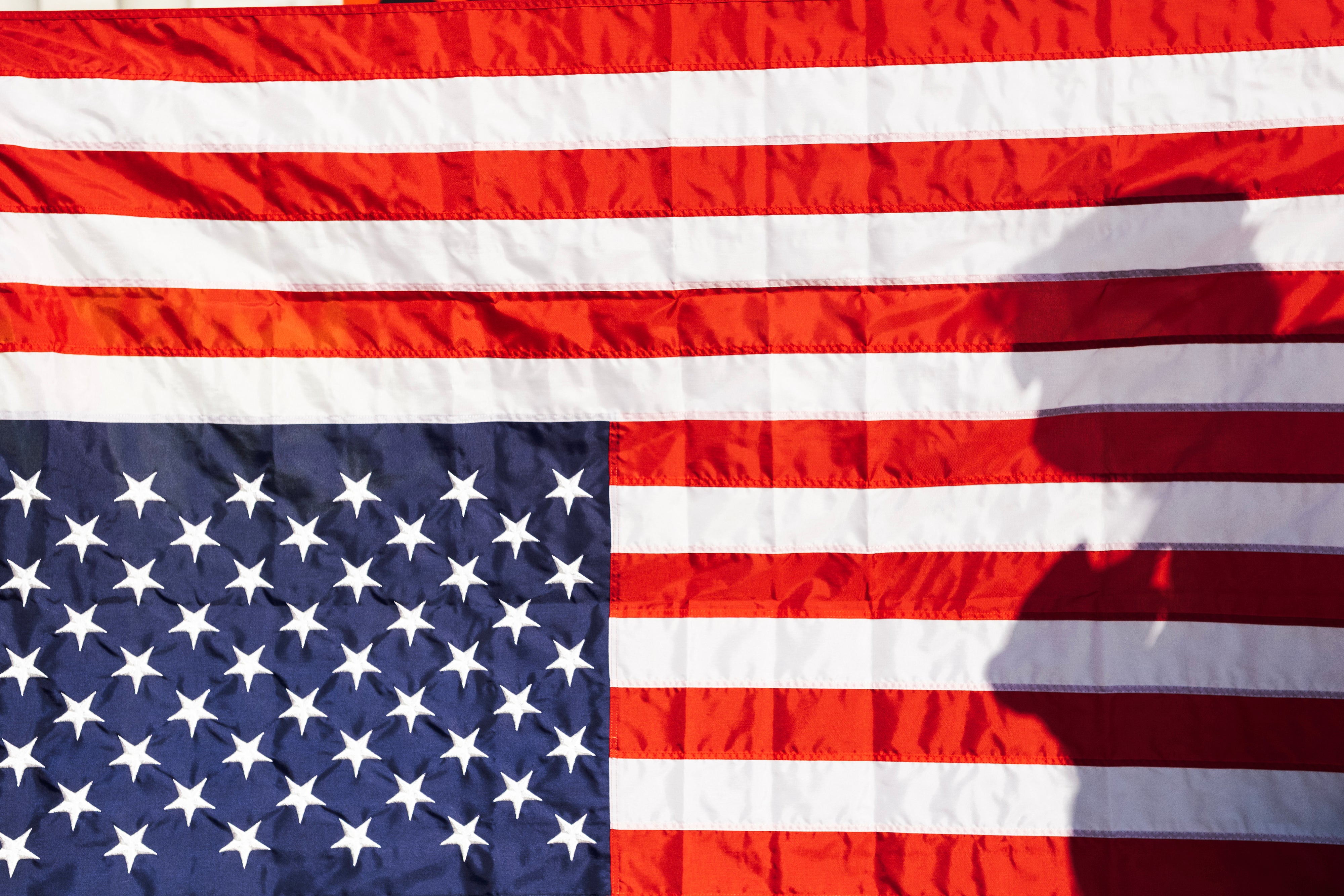 A protester is silhouetted on an upside-down American flag in front of City Hall