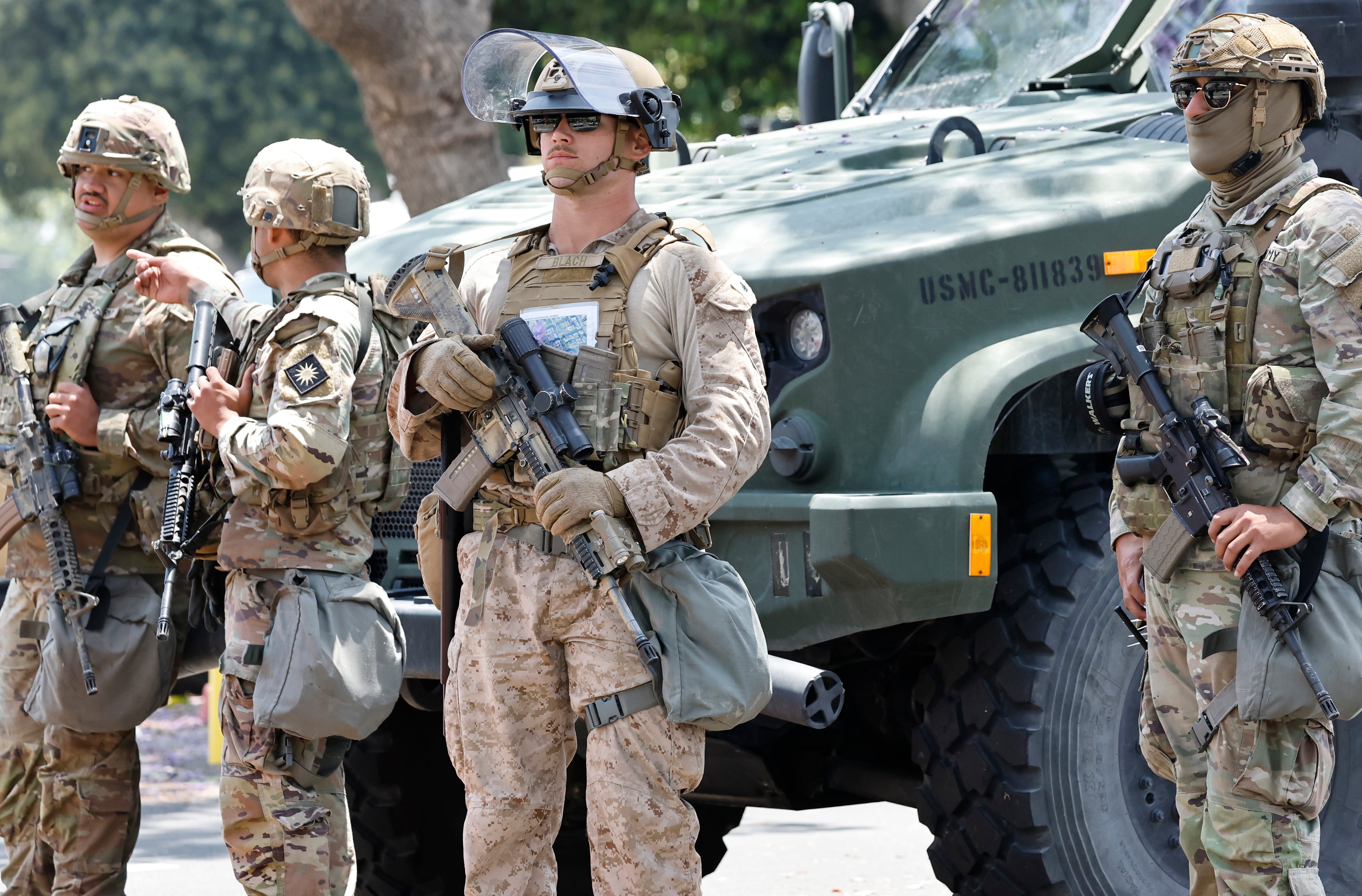 A U.S. Marine, center, and California National Guard soldiers guard an entrance to the Wilshire Federal Building, while standing by a U.S. Marine tactical vehicle on Friday in Los Angeles
