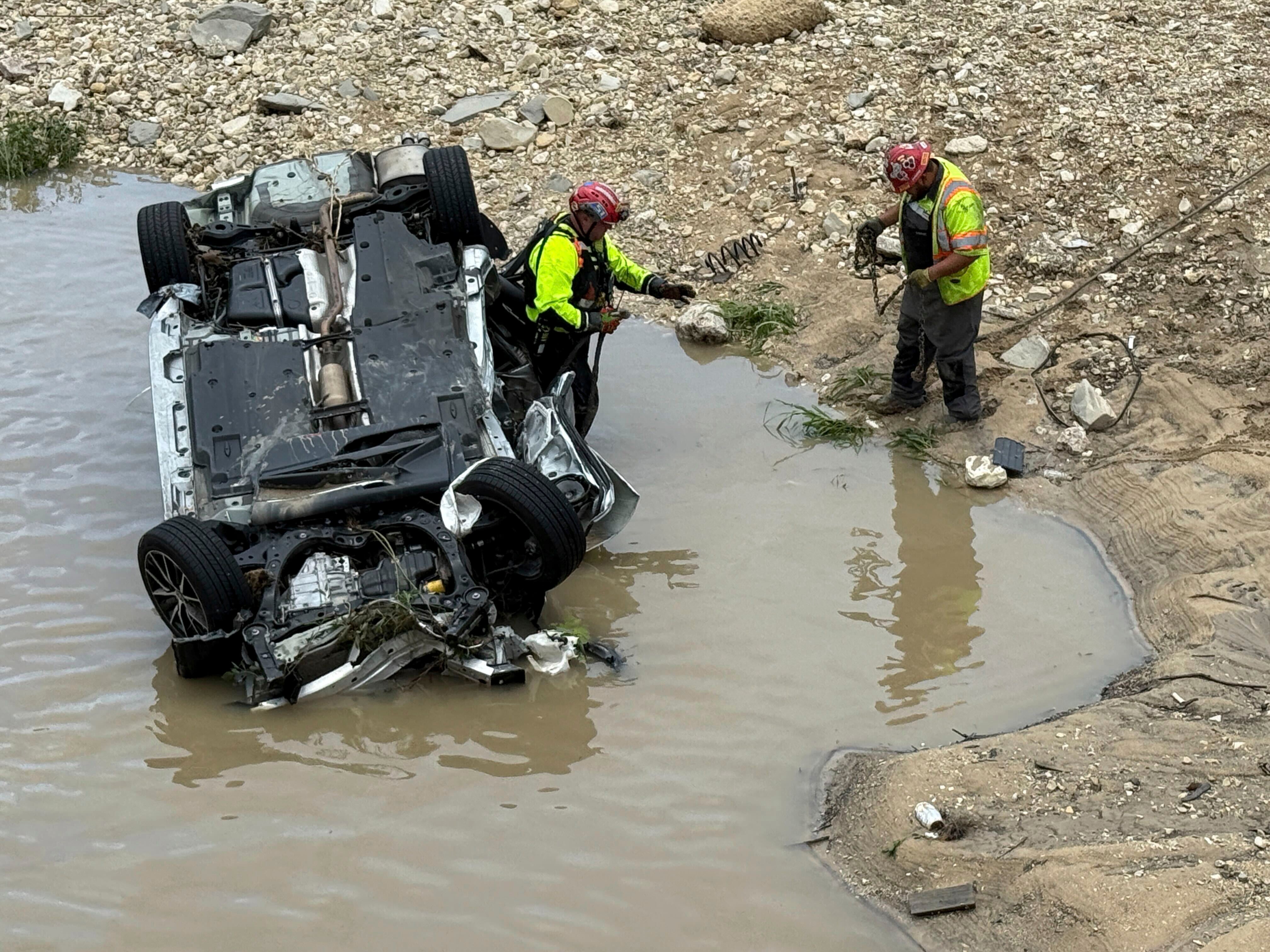 A crew works near a vehicle that was swept away in floodwaters in San Antonio on Thursday