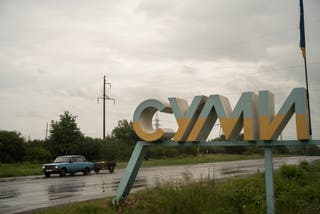 A Soviet-era car driving past a sign marking the northern entrance to the town of Sumy