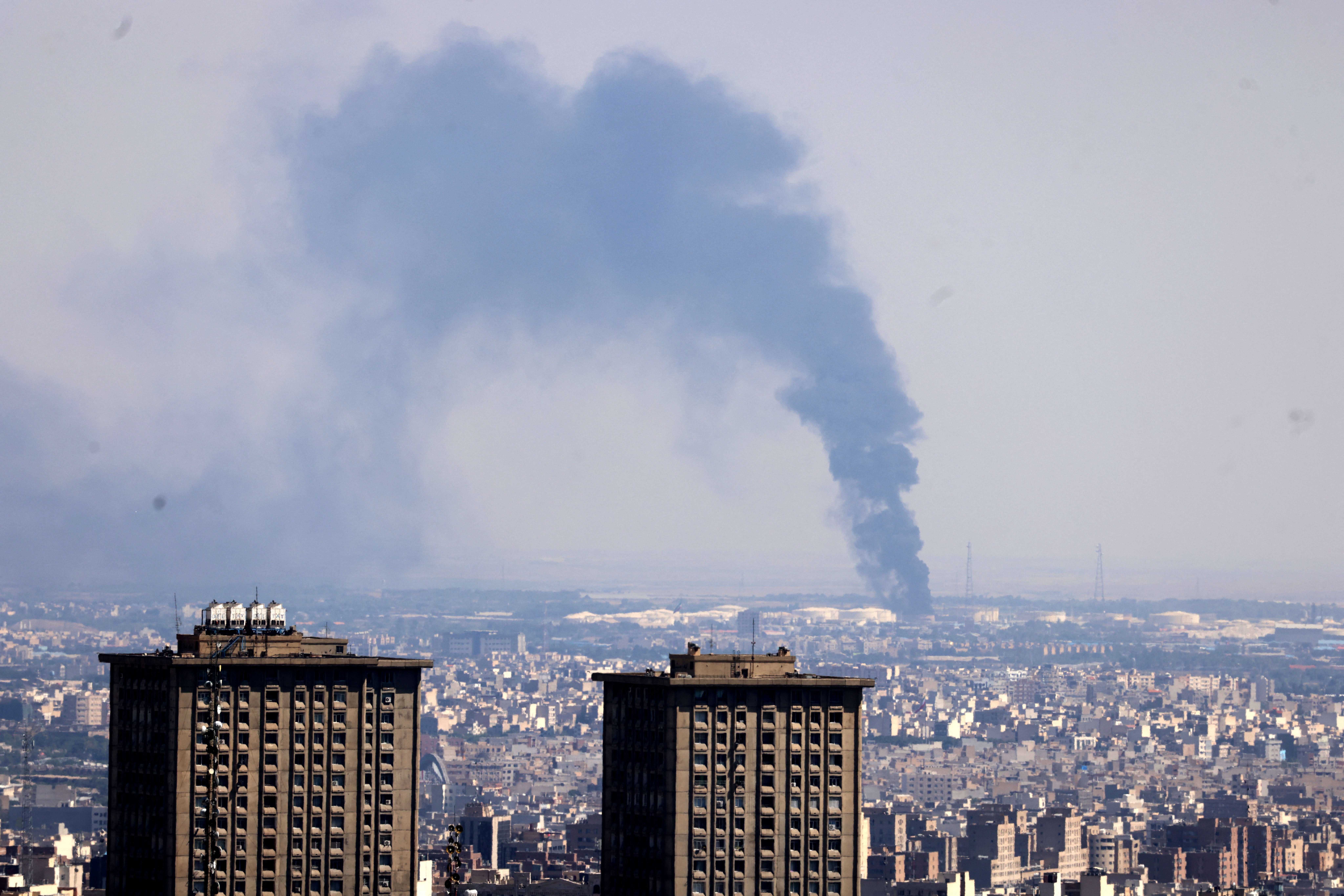 Smoke billows in the distance from an oil refinery following an Israeli strike on Tehran