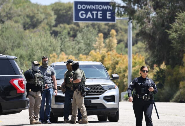 <p>An LAPD officer walks near masked federal agents staged outside a gate of Dodger Stadium on June 19, 2025 in Los Angeles, California</p>
