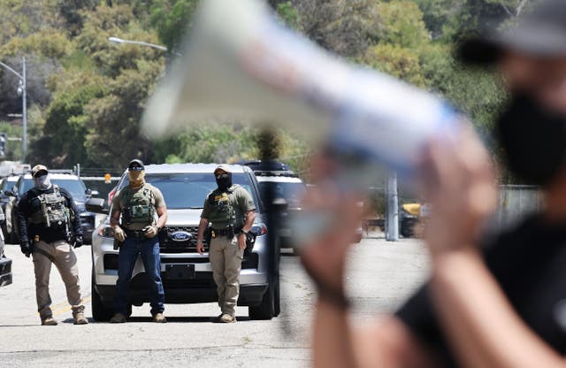 <p>A protester (R) demonstrates near masked federal agents staged outside a gate of Dodger Stadium on June 19, 2025 in Los Angeles, California</p>