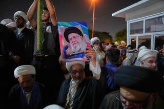 An Iraqi Shiite cleric holds a portrait of Iran's Supreme Leader Ali Khamenei during a protest against Israeli attacks