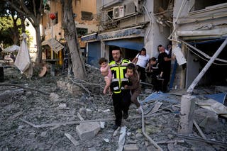 A rescue worker carries away children from the site of an Iranian missile strike in Haifa, Israel