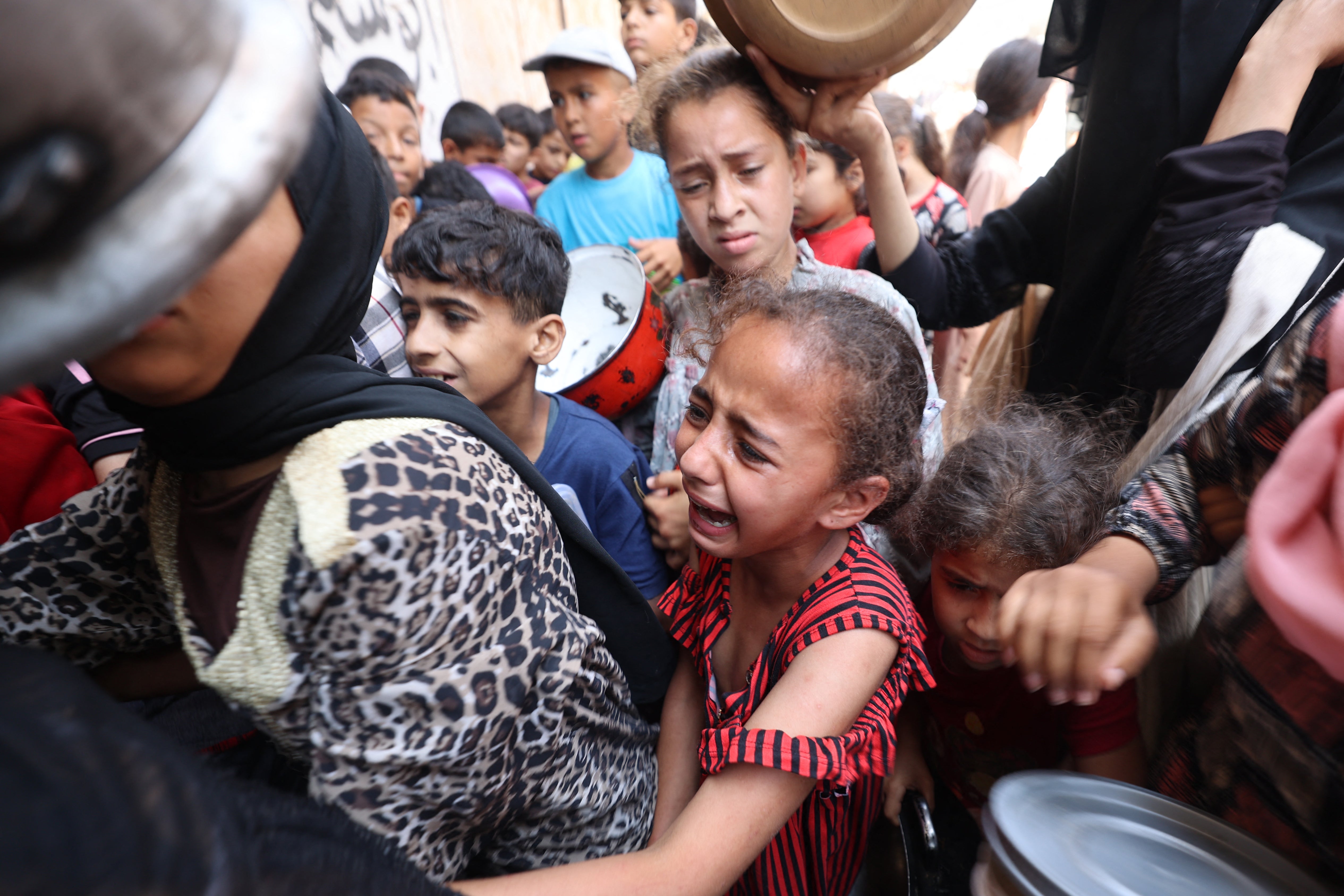 A Palestinian girl reacts as people queue at a food distribution point in Nuseirat, in the central Gaza Strip