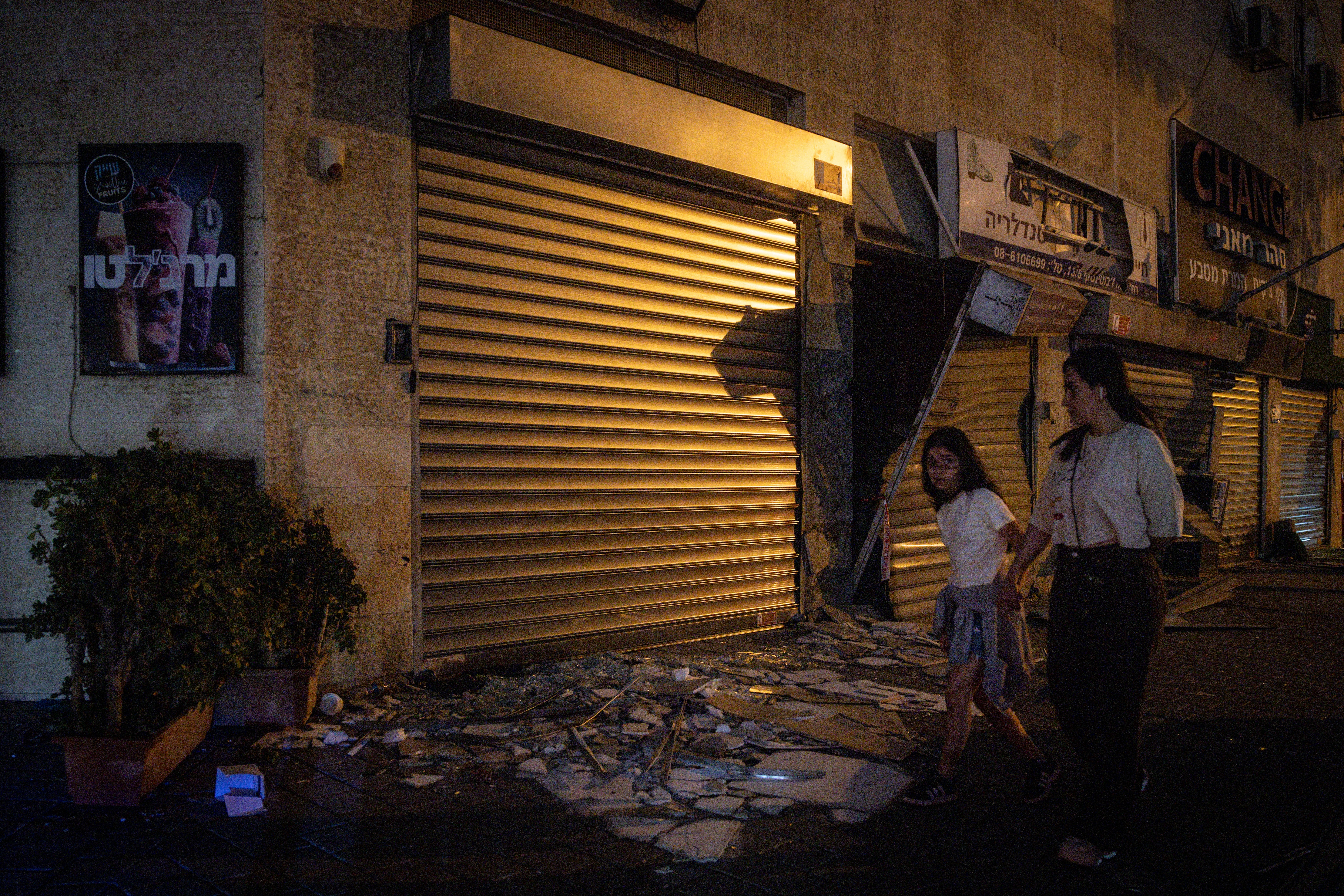 People walk past a damaged shop next to a building where four people were killed by an Iranian missile strike
