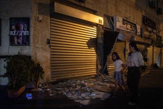 People walk past a damaged shop next to a building where four people were killed by an Iranian missile strike