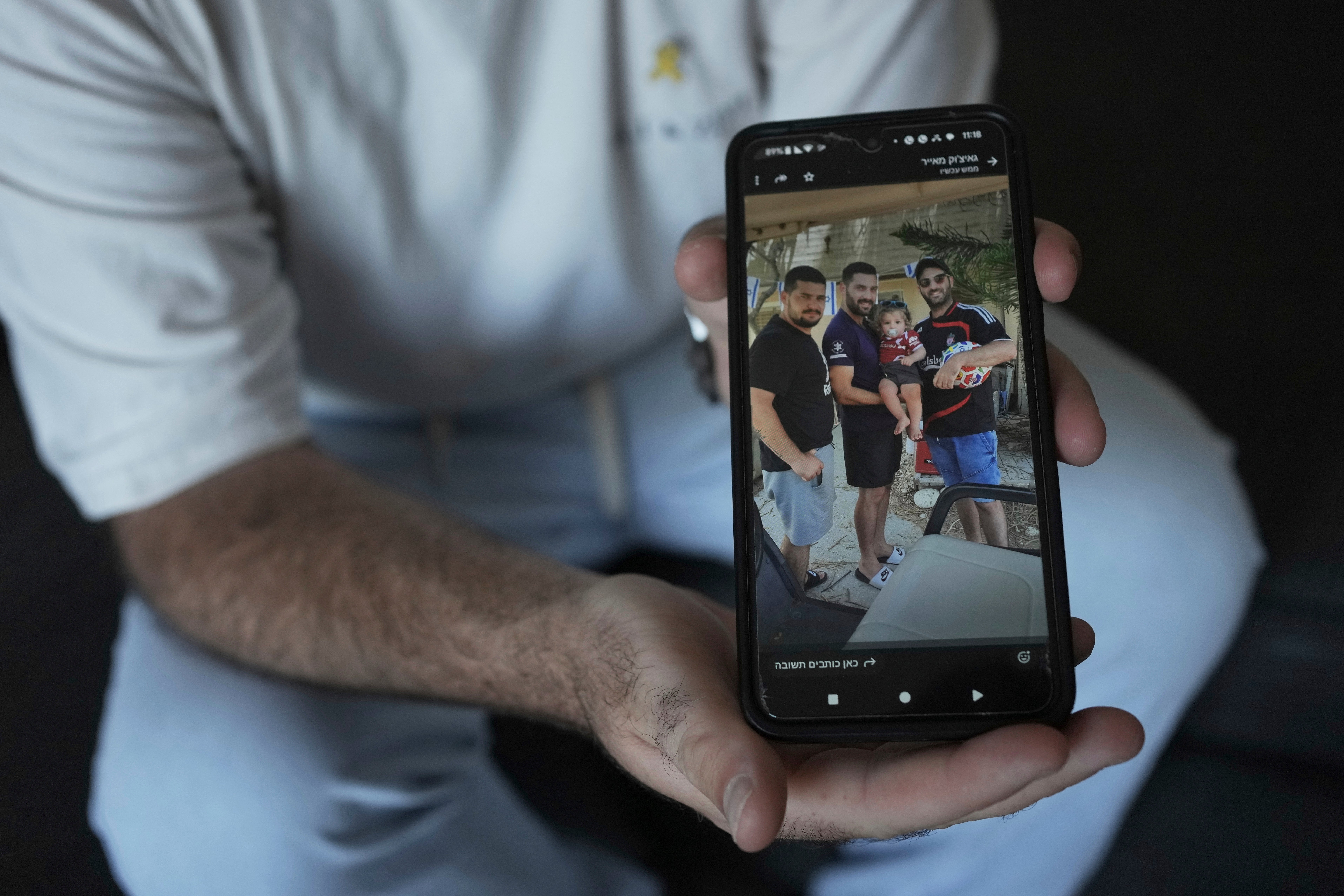 Liran Berman holds a picture on his mobile phone showing himself, right, and brothers, Ziv, left, and Gali, center, who were abducted by Hamas-led militants