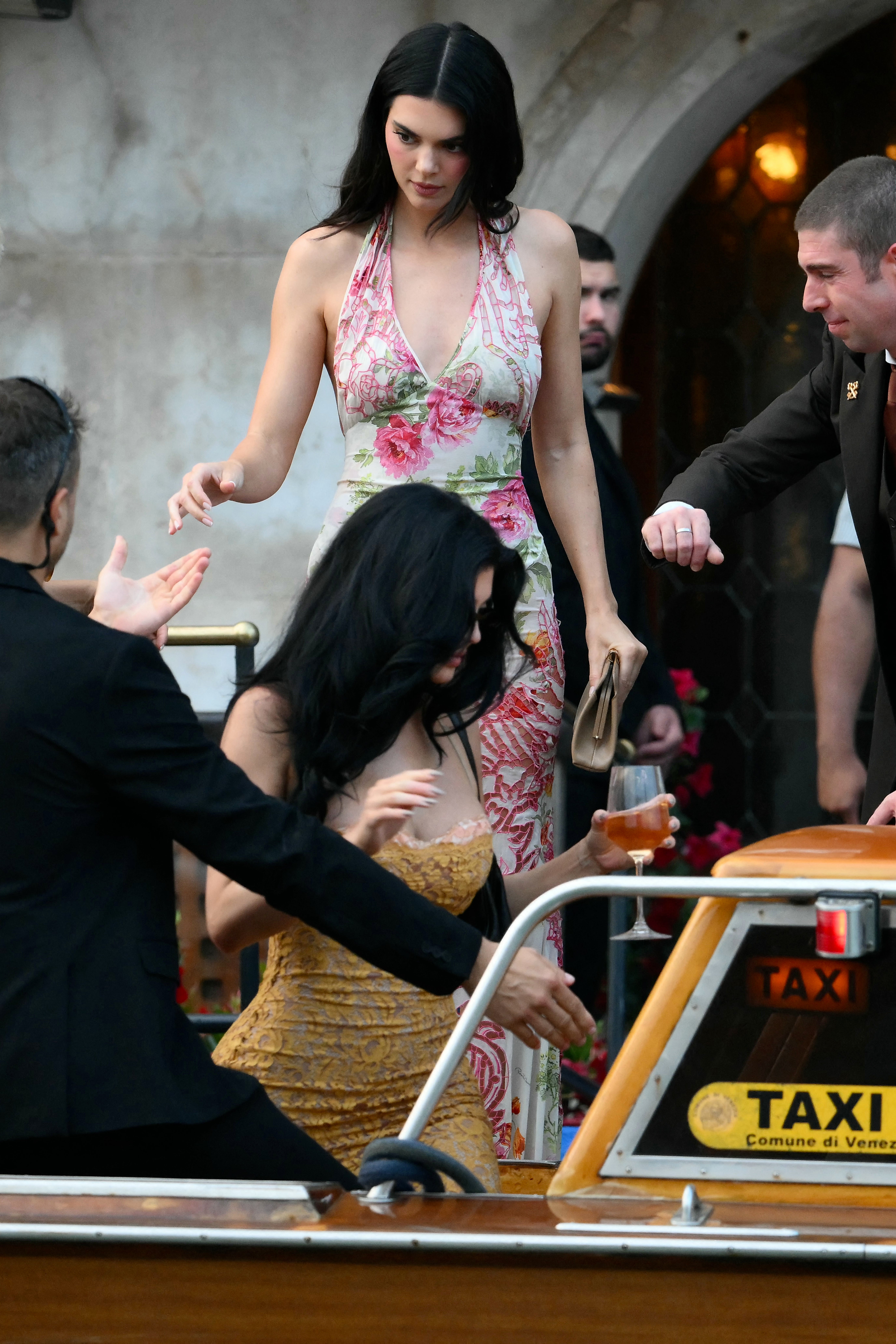 Kendall Jenner kicked off her ‘euro summer’ in the perfect halter dress. She headed to Bezos’ welcome party wearing a pink and green floral gown, with a tan clutch in hand