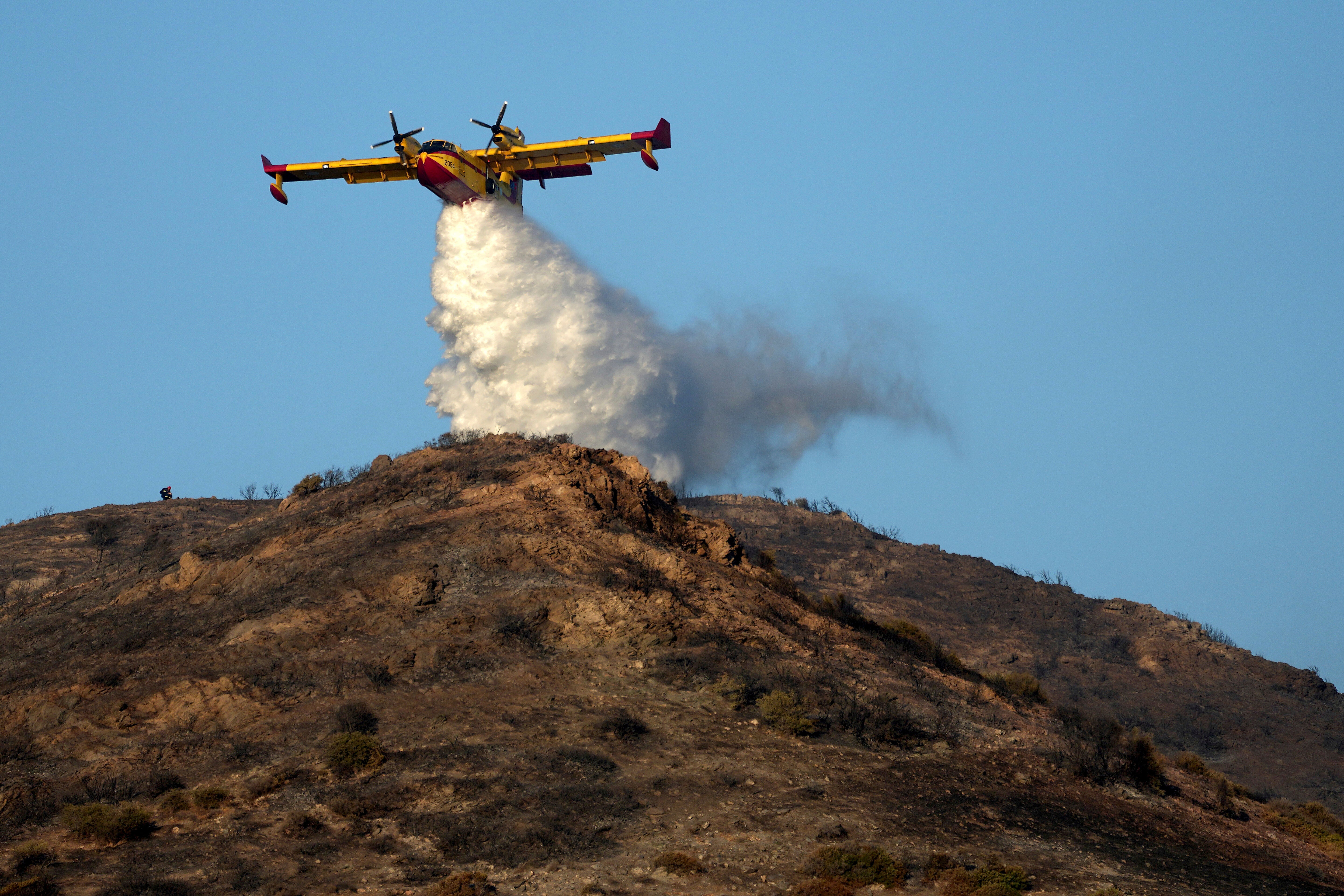 A firefighting airplane sprays water on a hill in Thymari, south of Athens