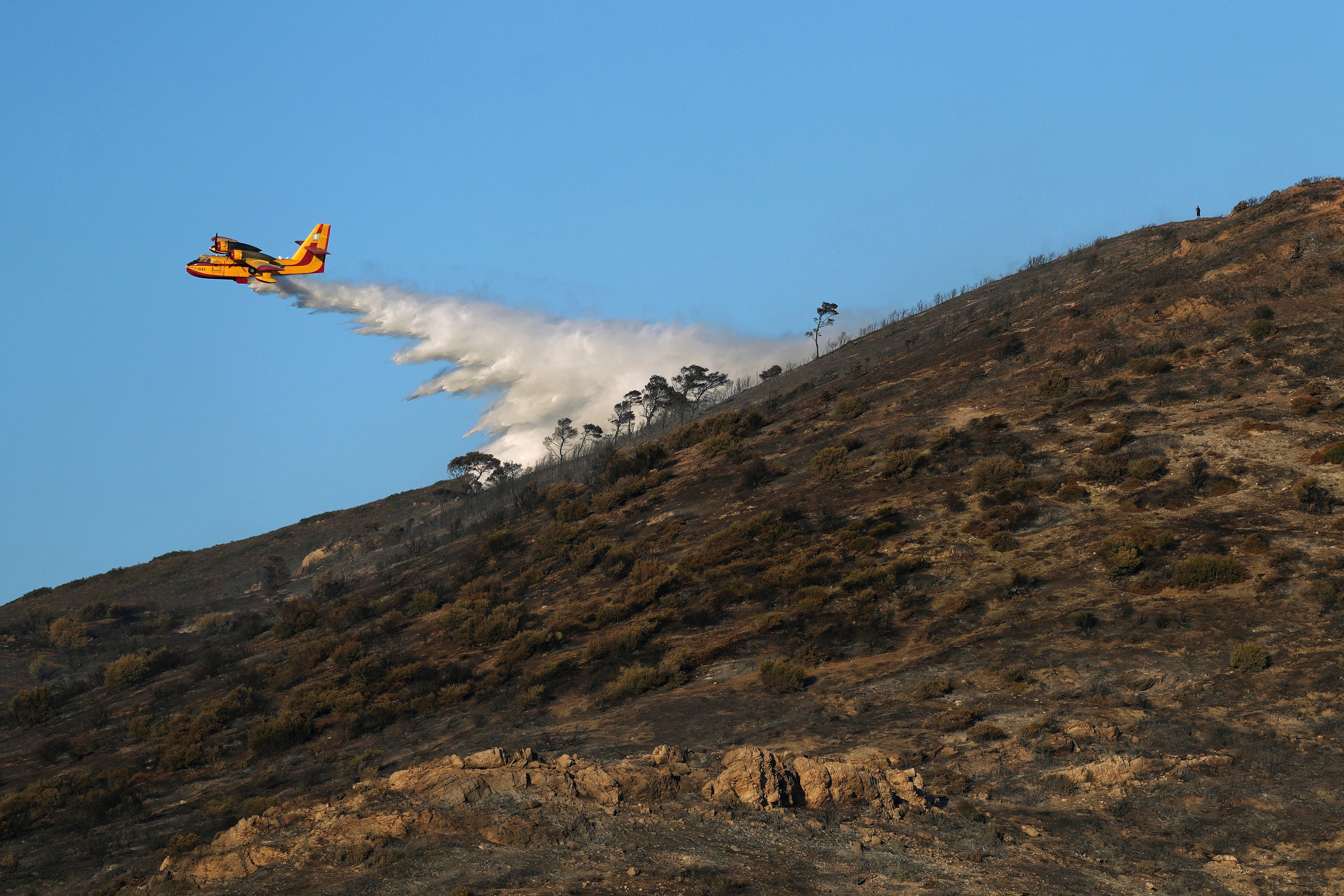 A firefighting airplane sprays water on a hill in Thymari, south of Athens