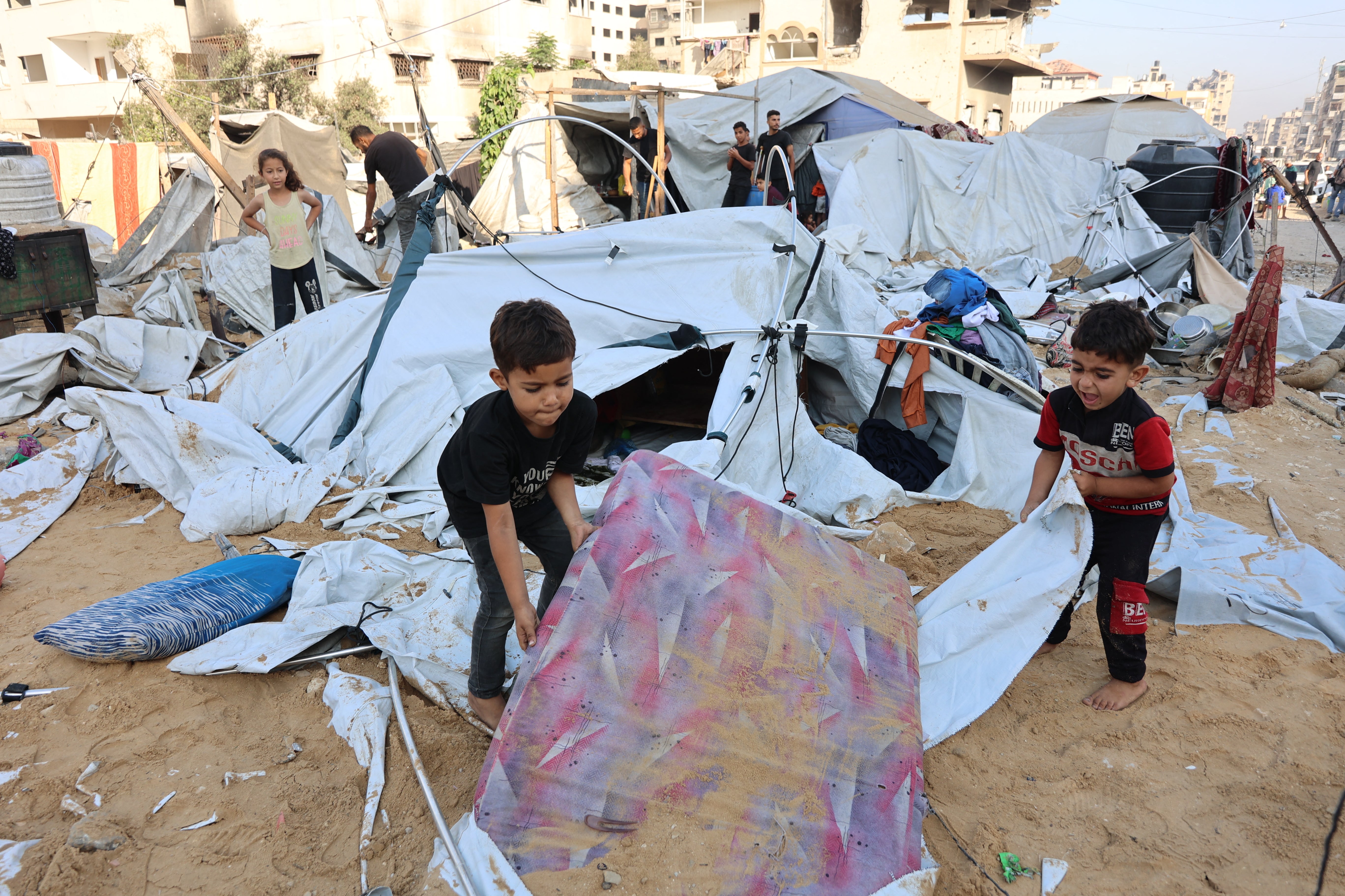 Palestinian little children lift a sand covered mattress after the Israeli army reportedly hit the tents of displaced people in the northern Al-Rimal neighborhood of Gaza City on June 28, 2025.