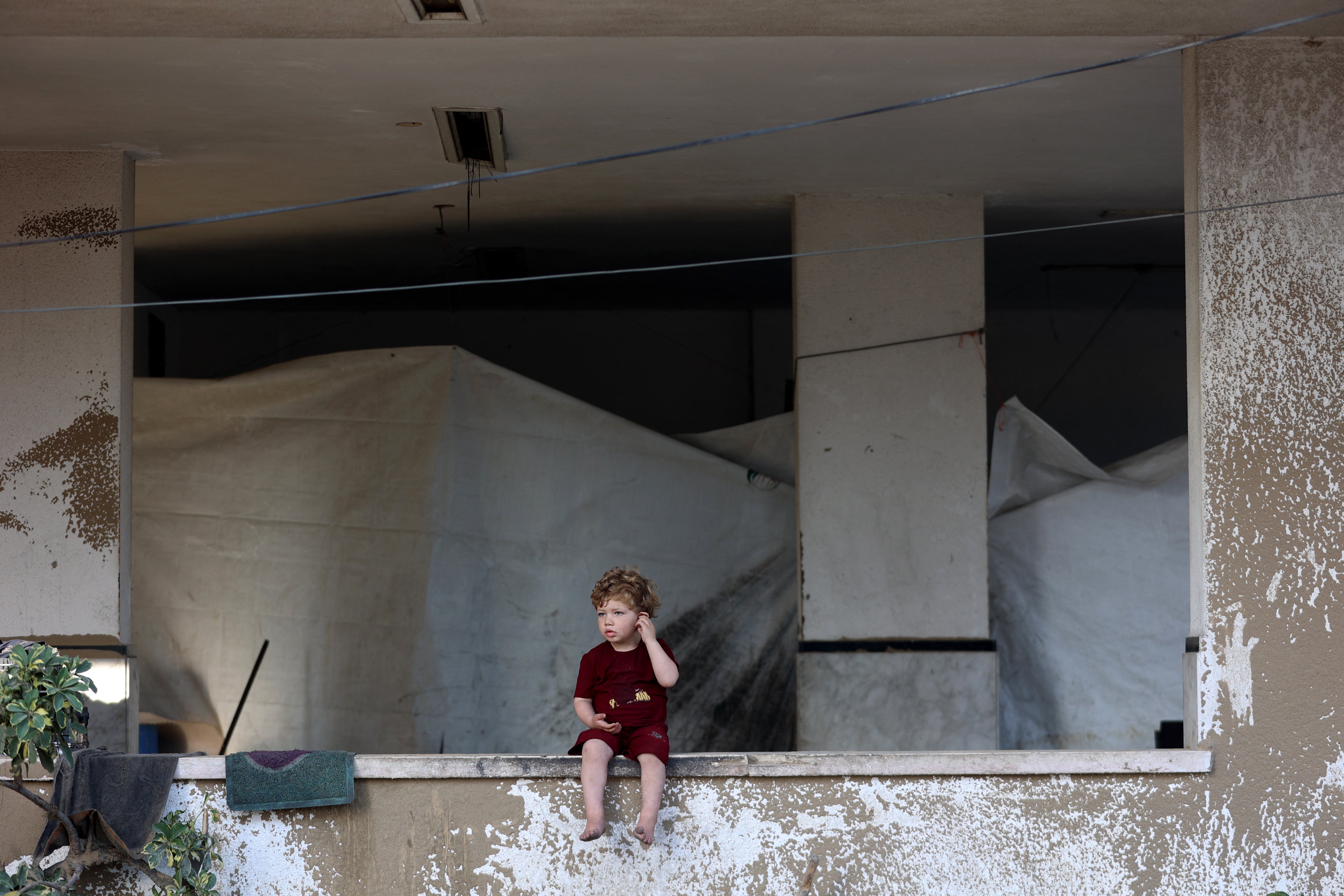 A tarpaulin shelter is setup under a building as a Palestinian child sits on a ledge after the Israeli army targeted the tents of displaced people in the northern Al-Rimal neighborhood of Gaza City on June 28, 2025.