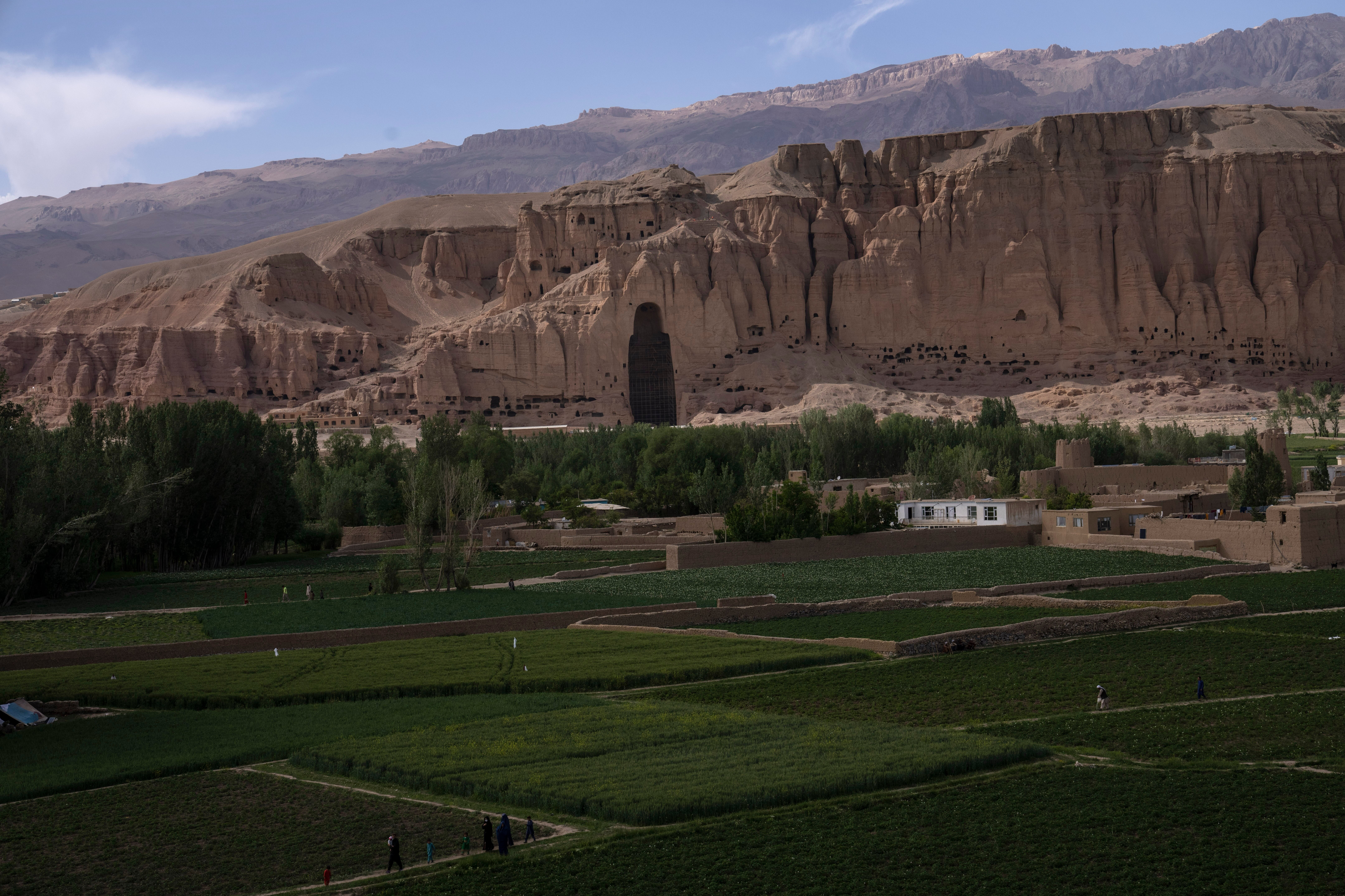 Villagers walk in the fields near the niche of the giant Buddha statue destroyed by the Taliban in 2001, in Bamiyan, Afghanistan, Saturday, June 17, 2023. (AP Photo/Rodrigo Abd,File