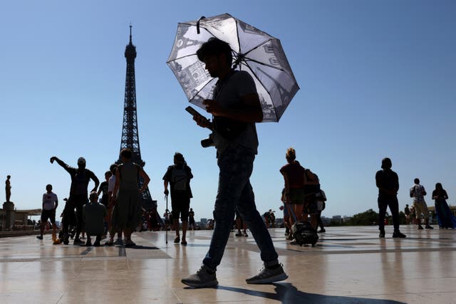 <p>A tourist holding an umbrella to protect himself from the sun walks at Trocadero square next to the Eiffel Tower</p>
