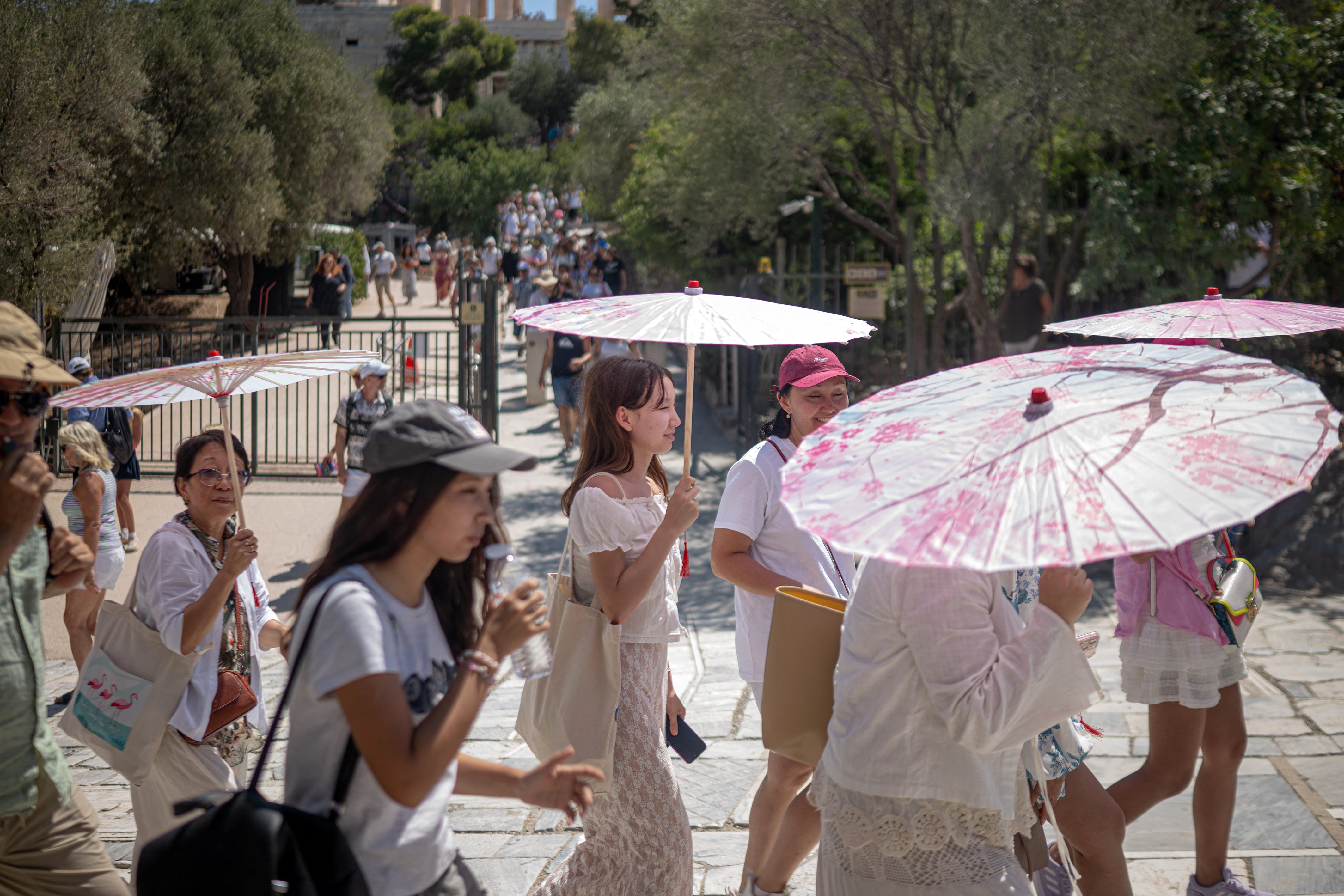 Tourists protect themselves from the sun with umbrellas while waiting to get access to the Acropolis hill in Athens