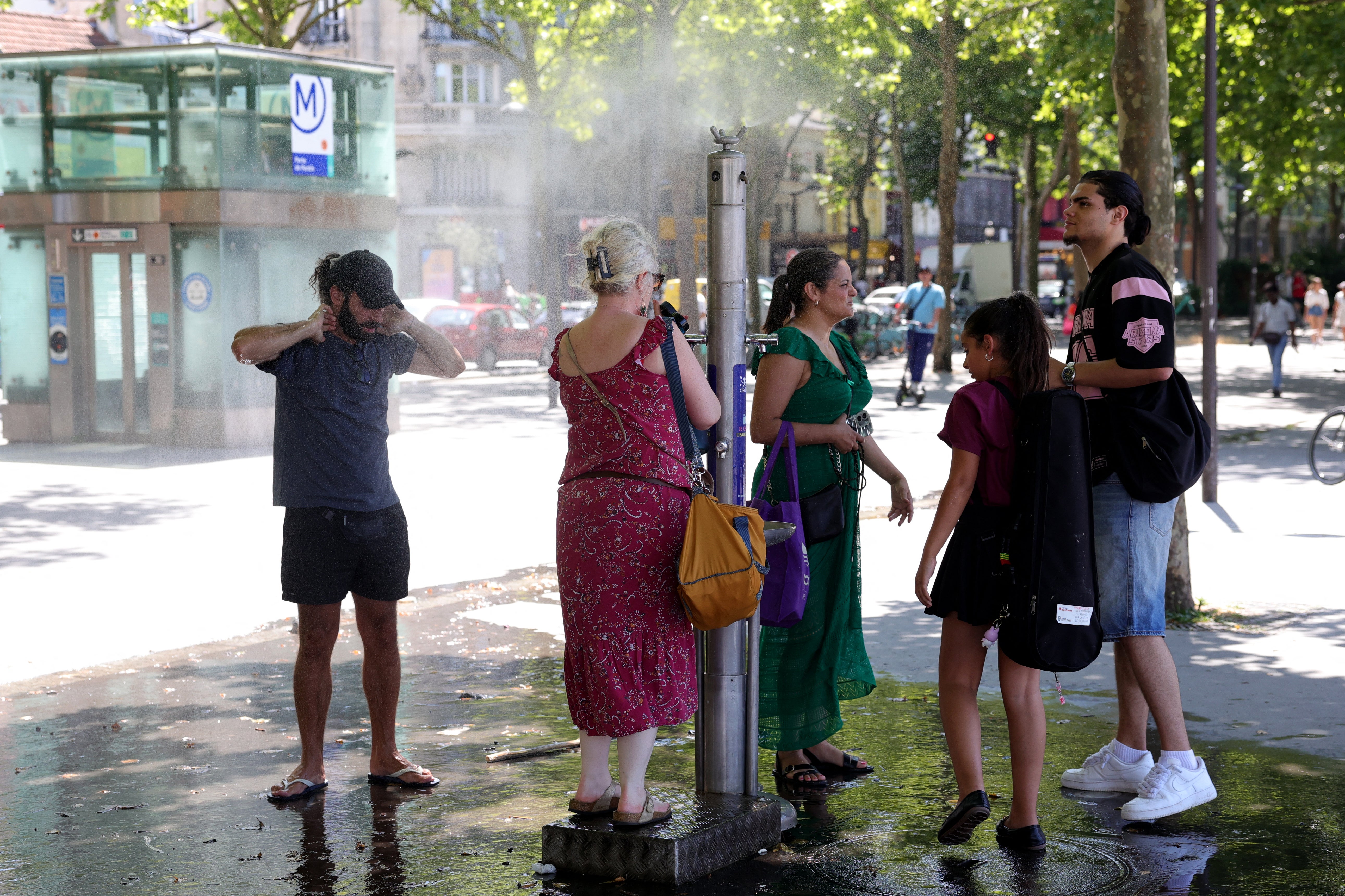 Pedestrians cool off with a public water jet in a street during a heatwave in Paris on June 21, 2025