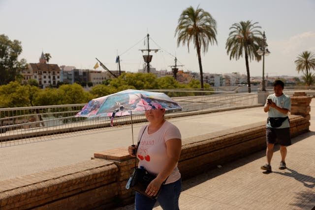 <p>A woman holds an umbrella to shield herself from the strong sun during a heatwave in Seville, Spain</p>