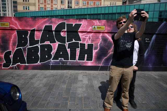 <p>Fans take selfies in front of a mural painted in honour of rock band Black Sabbath ahead of their Birmingham concert</p>