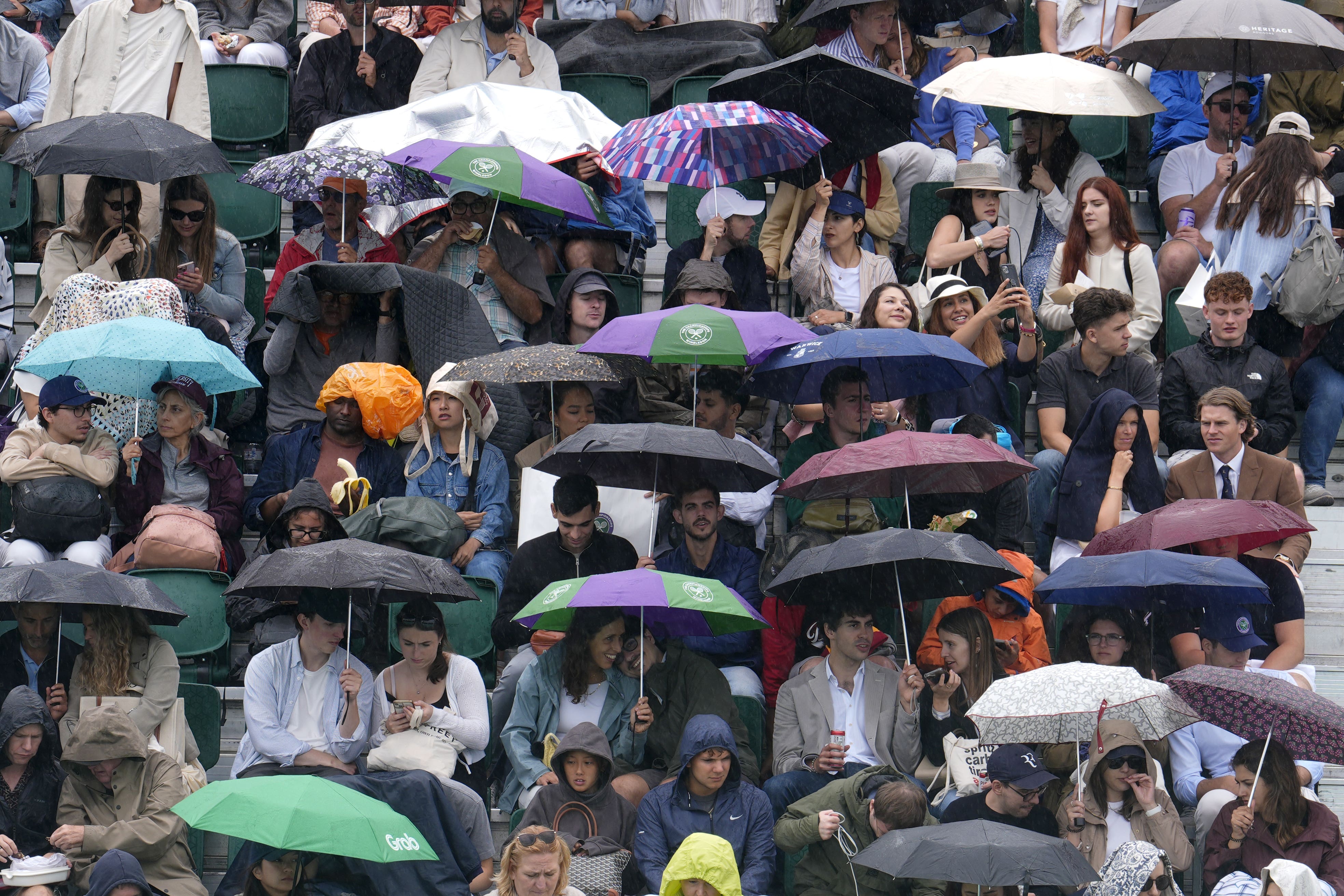 Spectators shelter form the rain on day six of the 2025 Wimbledon Championships at the All England Lawn Tennis and Croquet Club (Jordan Pettitt/PA)