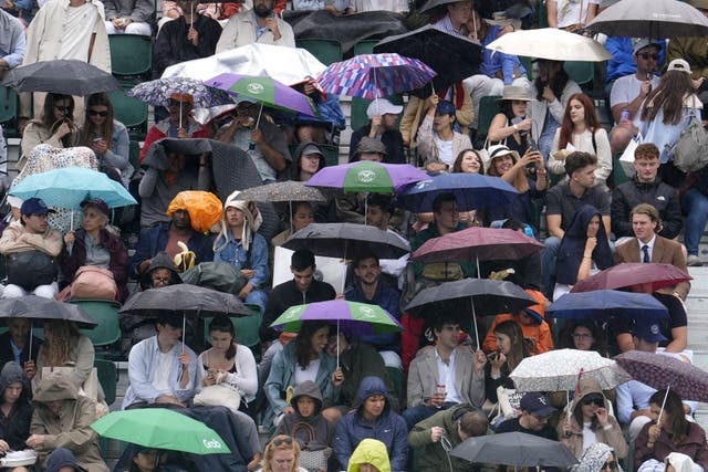 Spectators shelter form the rain on day six of the 2025 Wimbledon Championships at the All England Lawn Tennis and Croquet Club (Jordan Pettitt/PA)