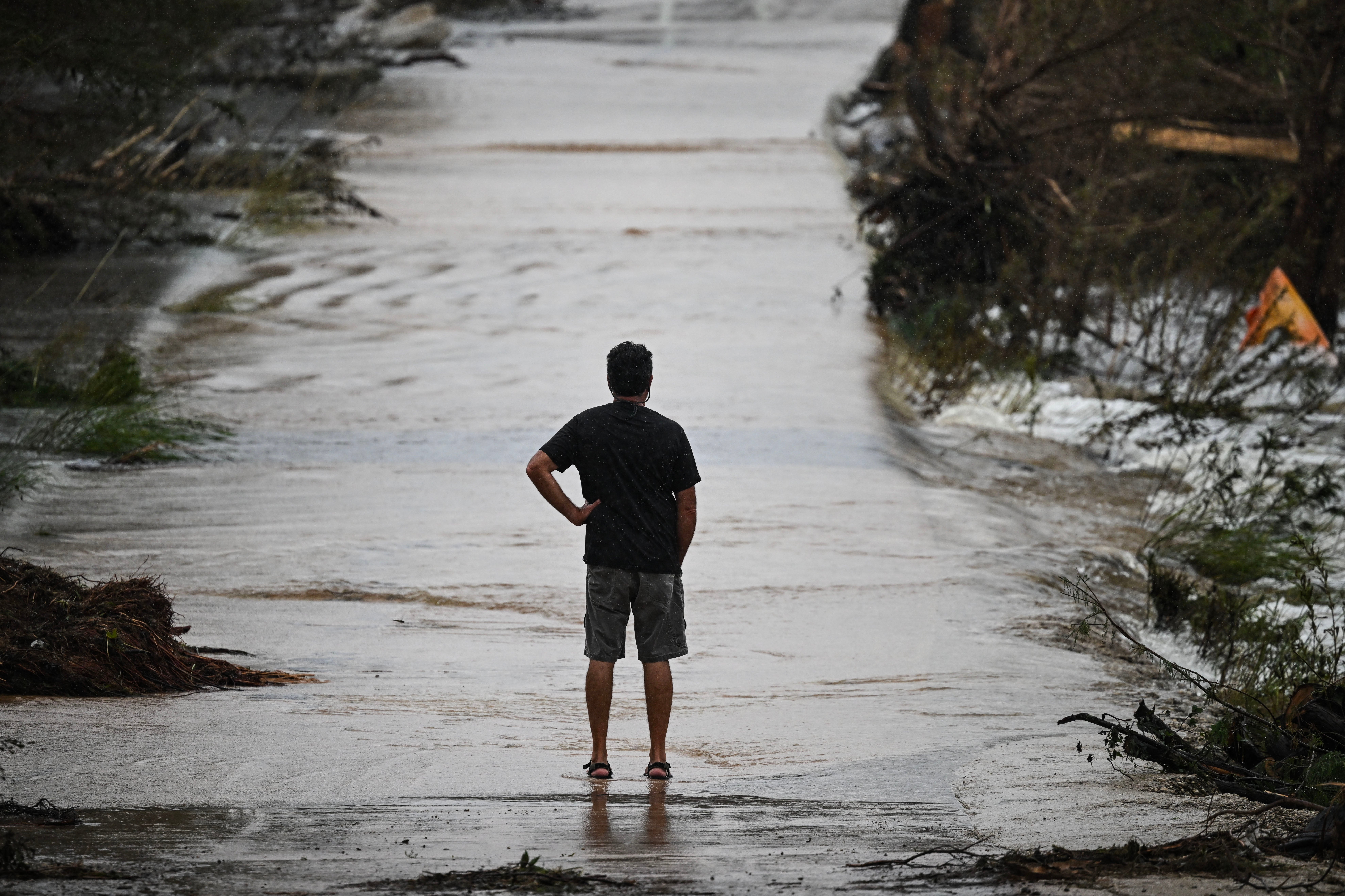 A man looks at a damaged road after severe flash flooding that occurred during the July 4 holiday weekend, in Hunt, Texas, on July 6, 2025. Rescuers in Texas raced against time Sunday to find dozens of missing people, including children, swept away by flash floods that killed at least 59, as forecasters warned of new deluges. Local Texans joined forces with disaster officials to search through the night for the missing, including 27 girls from a riverside Christian summer camp. Texas Governor Greg Abbott said Camp Mystic on the banks of the Guadalupe River, where some 750 girls had been staying when the floodwaters hit, had been "horrendously ravaged in ways unlike I've seen in any natural disaster." (Photo by RONALDO SCHEMIDT / AFP) (Photo by RONALDO SCHEMIDT/AFP via Getty Images)