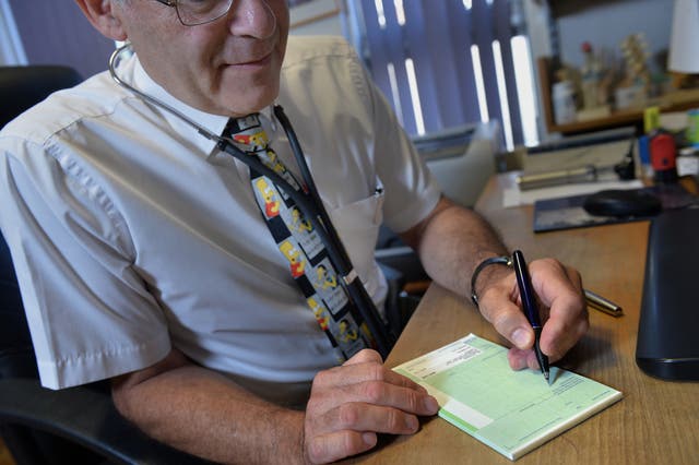 <p>A GP writes a prescription in his practice room at the Temple Fortune Health Centre GP Practice near Golders Green, London</p>