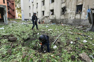 Police officers clear the debris resulting from a Russian drone strike near a damaged residential building in Kharkiv