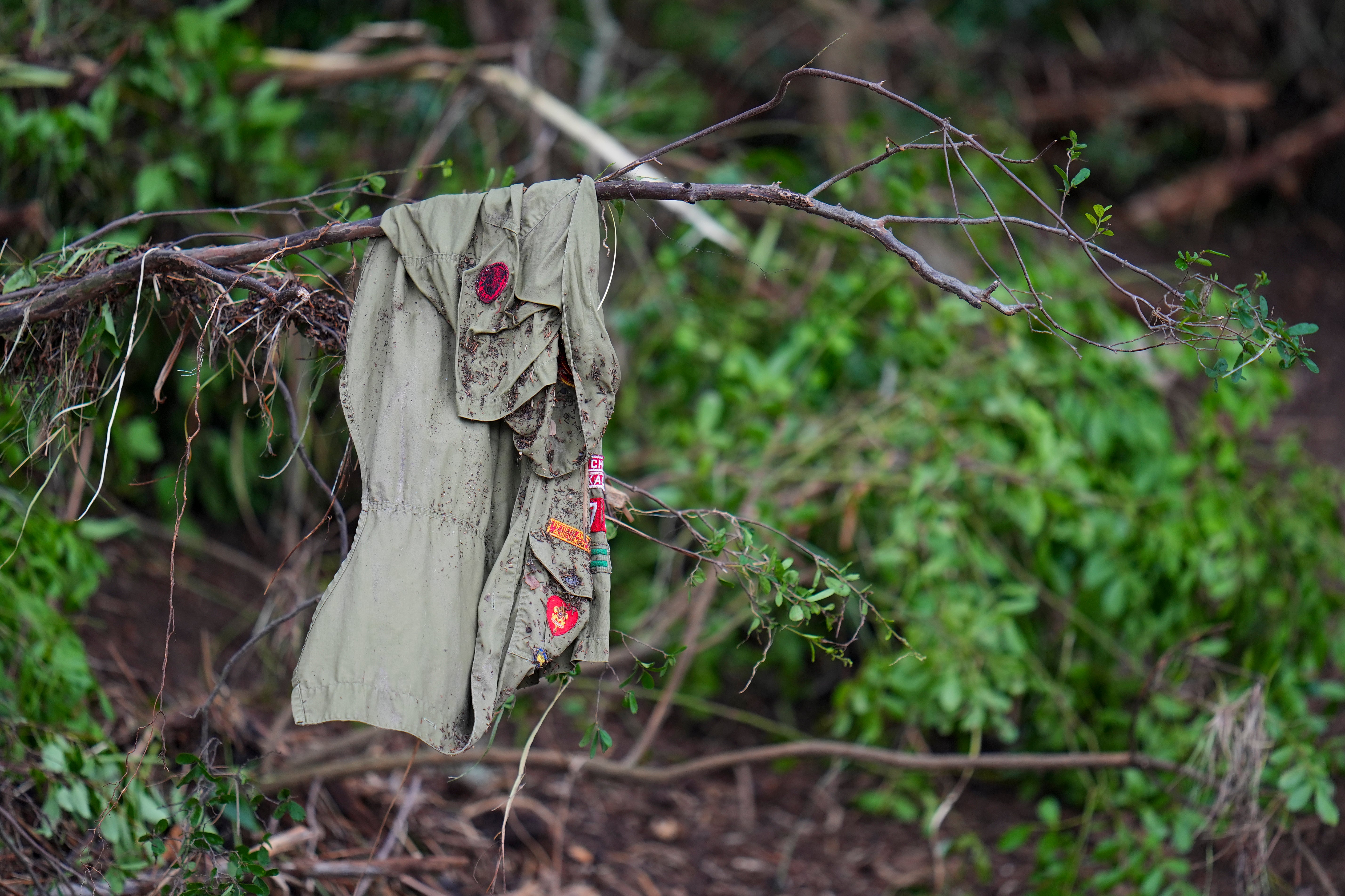 Patches cover a shirt hanging on a tree, across the Guadalupe River from Camp Mystic