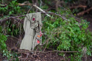 Patches cover a shirt hanging on a tree, across the Guadalupe River from Camp Mystic