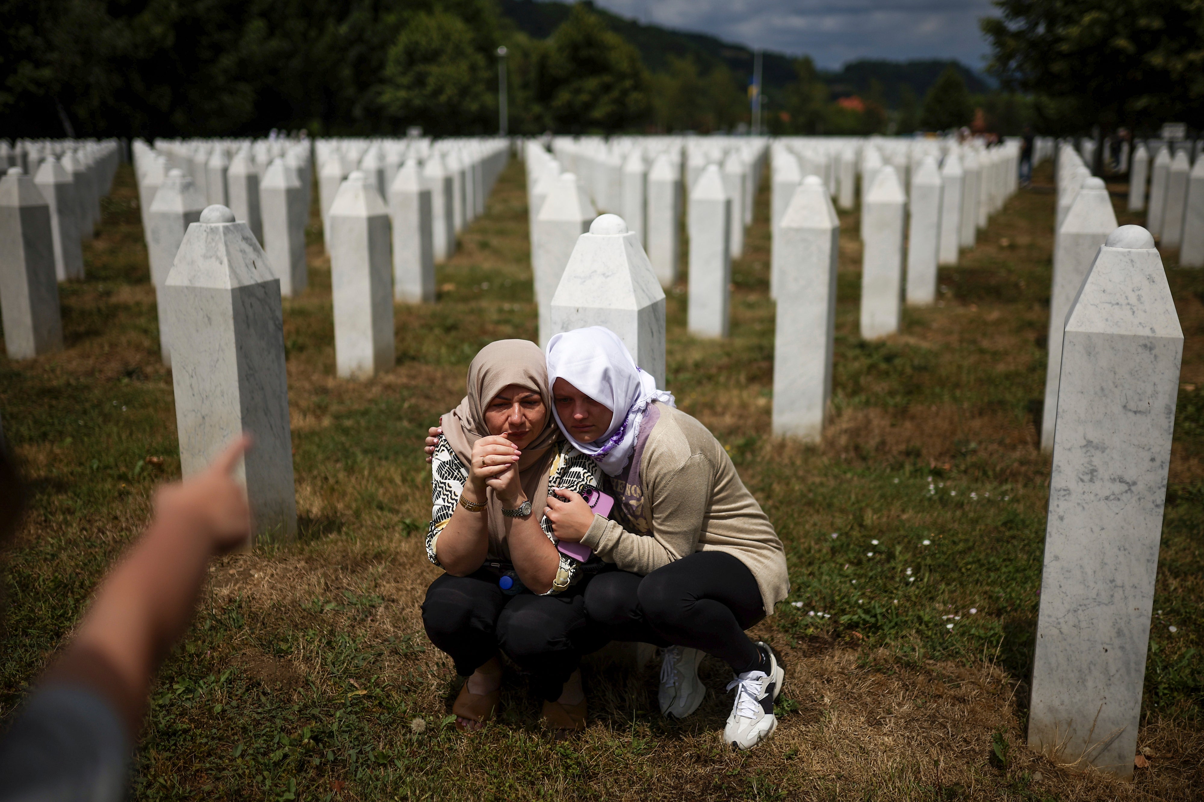 Family members mourn beside the grave of their cousin, victims of Srebrenica genocide