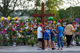 Dan Beazley, left, holds a large cross as he prays with visitors at a memorial for flood victims on Thursday