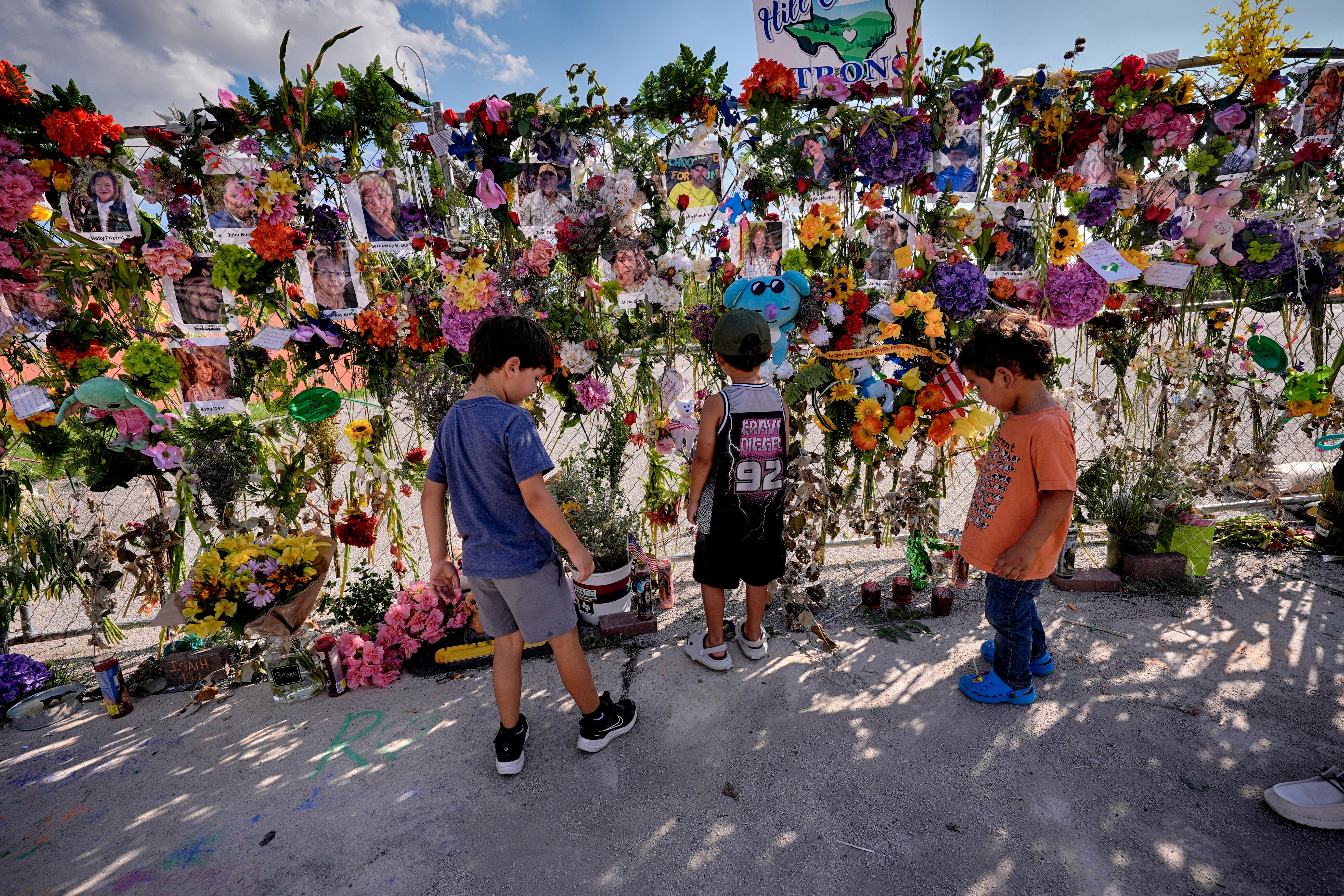 Children stand by the memorial wall of flowers and photos of flood victims prior to the vigil on Friday in Kerrville, Texas