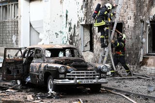 Firefighters are seen next to a burnt-out car following mass Russian drone and missile strikes in the western Ukrainian city of Lviv