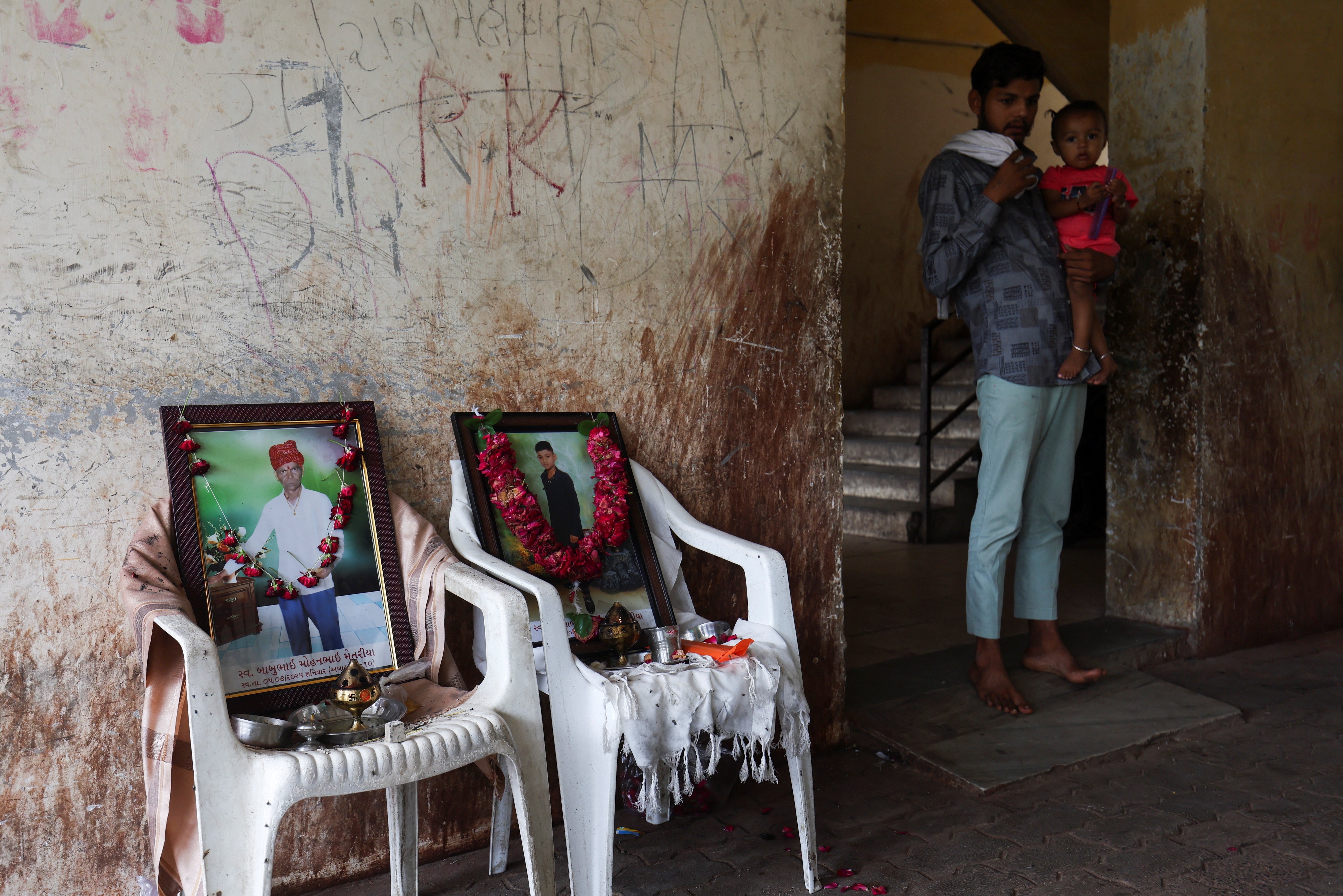 A family member with a child, stands next to photo of Akash Patni, who died after an Air India Boeing 787-8 Dreamliner plane crashed during takeoff from an airport, in Ahmedabad