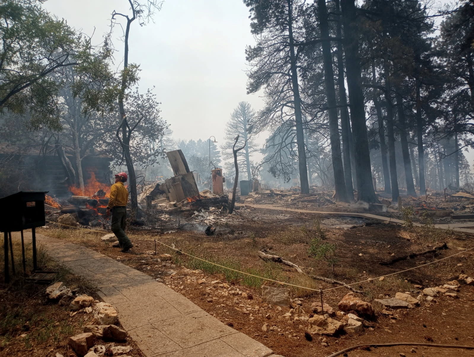 A firefighter stands near smoldering debris and active flames amid the charred remains of a burned structure near the Grand Canyon Lodge in Arizona, U.S. July 13, 2025. National Park Service/Handout via REUTERS