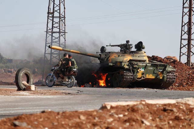 <p>Syrian government soldiers on a motorcycle pass by a burning tank on the outskirts of Sweida city on Monday</p>