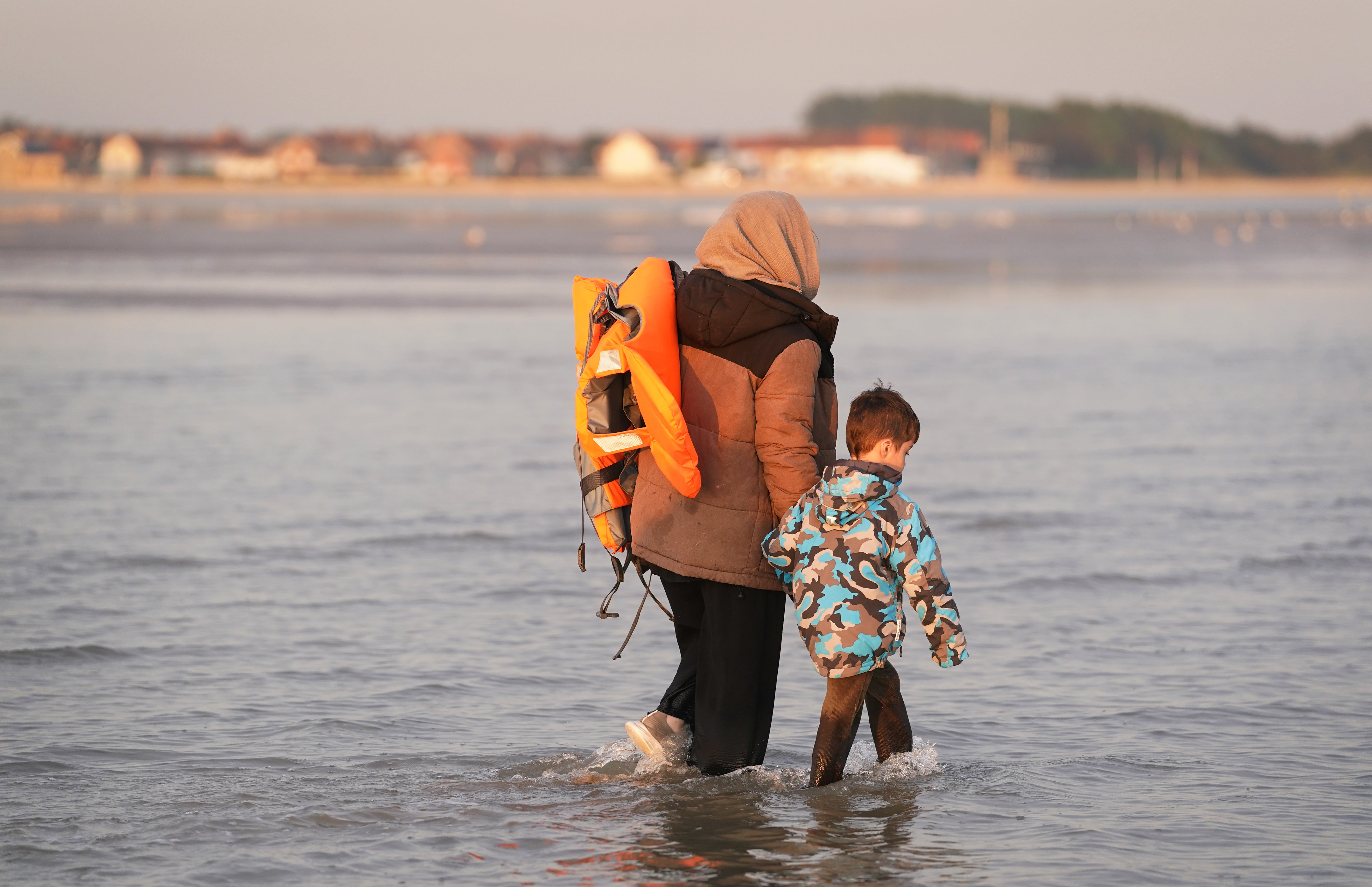<p>A mother and son, thought to be migrants, wade into the sea to board a small boat (Gareth Fuller/PA)</p>