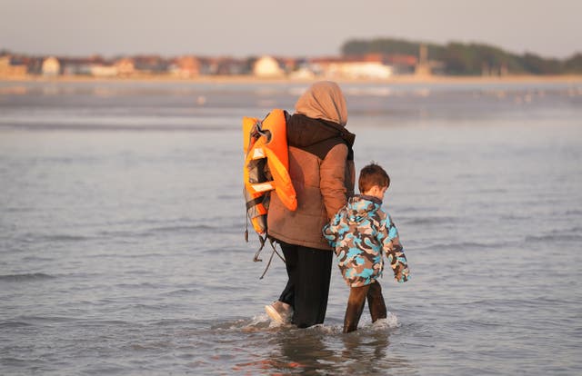 <p>A mother and son, thought to be migrants, wade into the sea to board a small boat (Gareth Fuller/PA)</p>